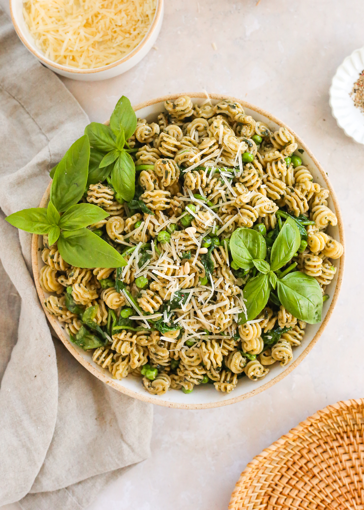 A large ceramic serving bowl filled with a freshly made basil pesto pasta, garnished with fresh basil leaves and shredded Parmesan cheese.
