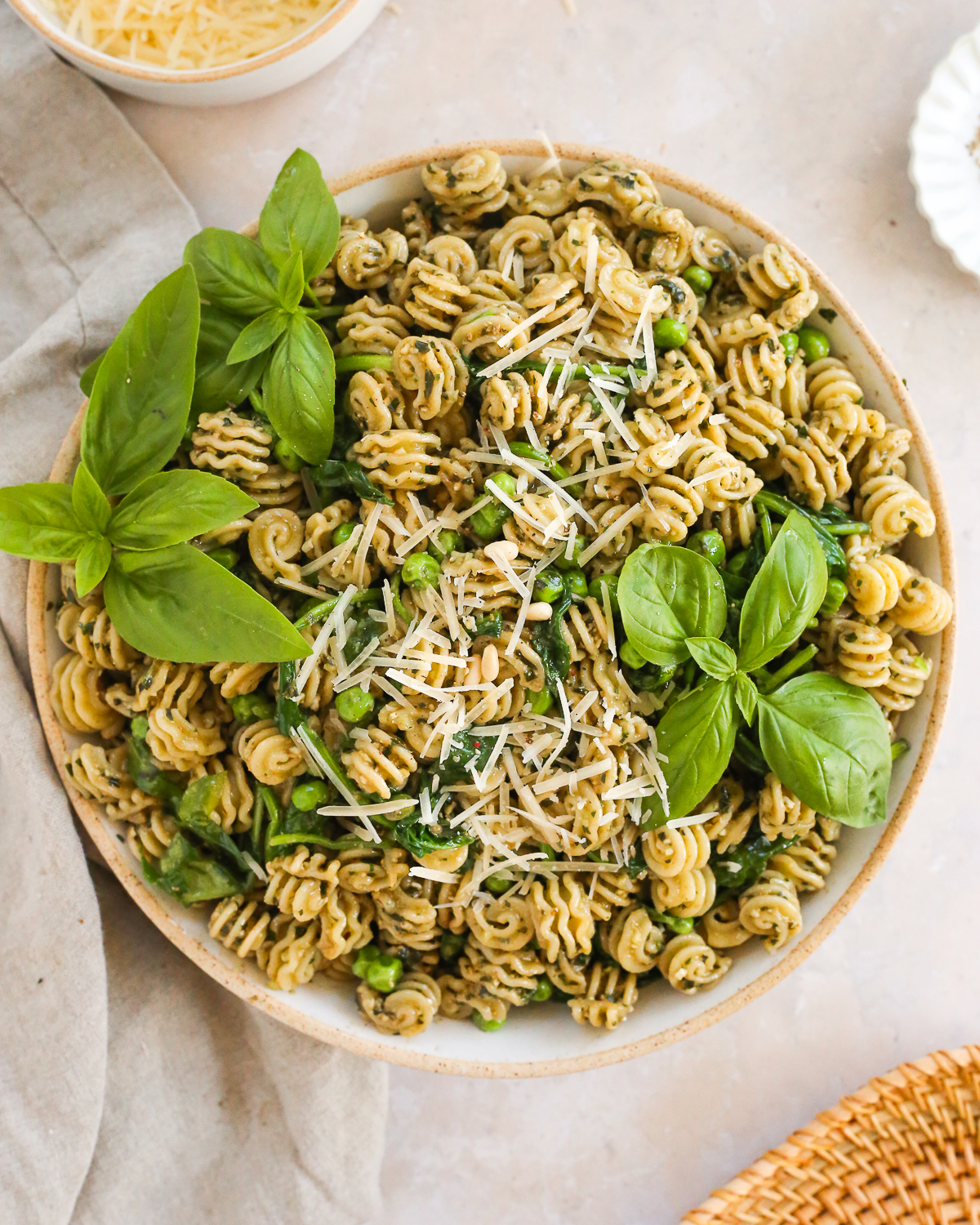 A large serving bowl filled with Basil Pesto Pasta, garnished with fresh basil and shredded Parmesan cheese. 