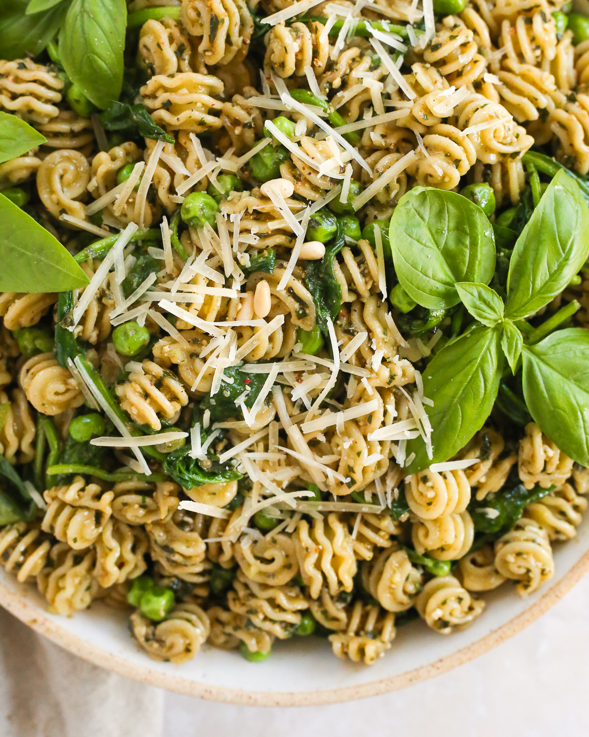 A close view of freshly cooked pasta tossed with a basil pesto sauce, garnished with fresh basil and shredded Parmesan cheese.