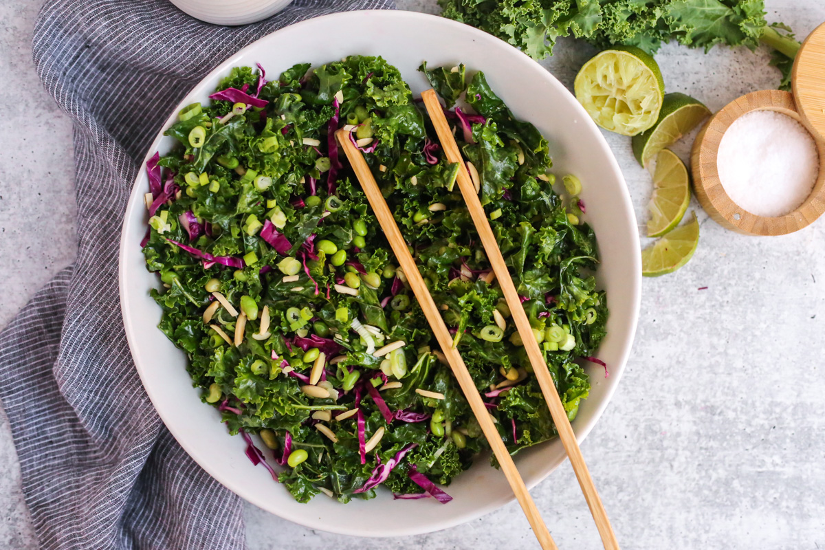 Overhead view, portrait orientation, of a colorful and fresh massaged kale salad with sesame lime dressing