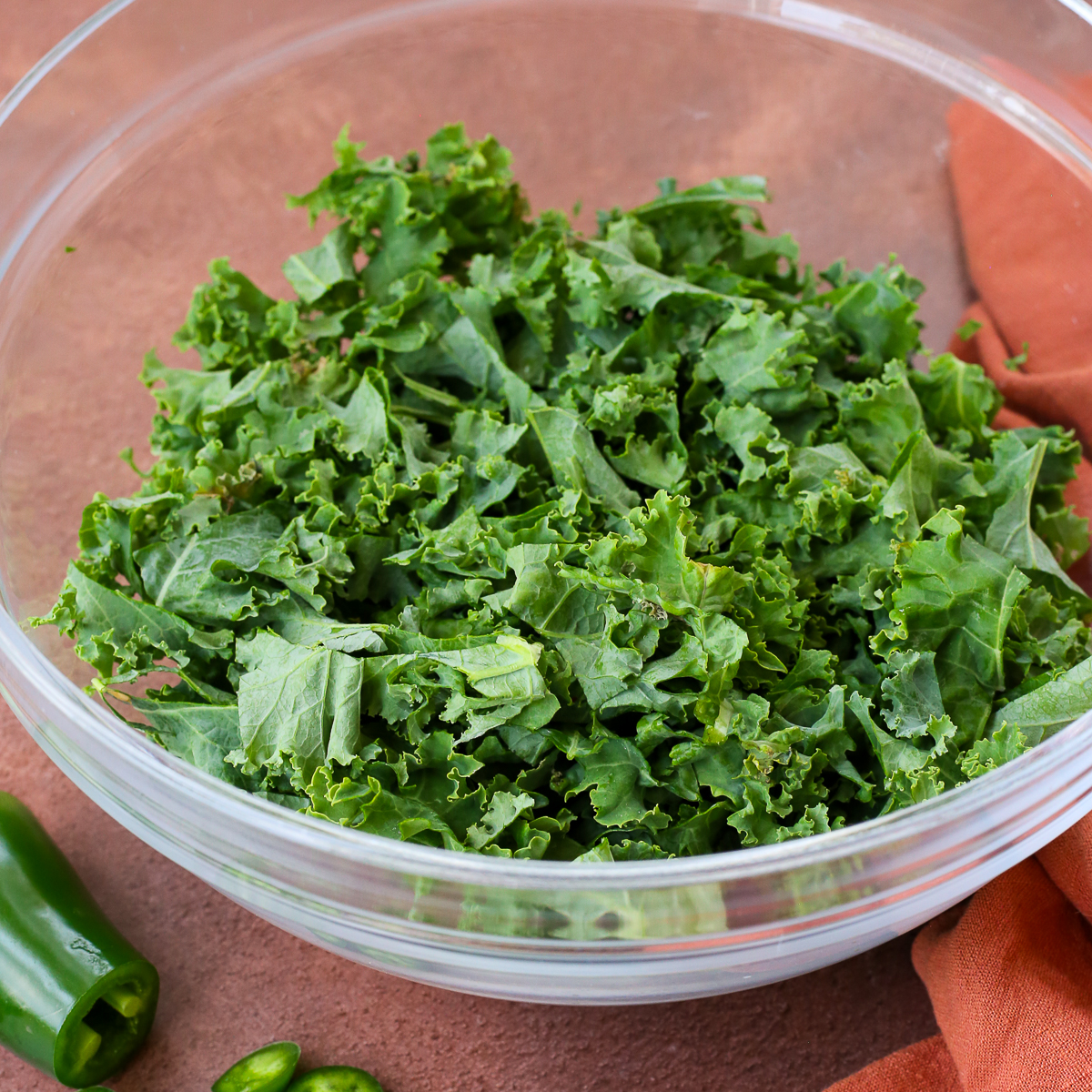 A large glass mixing bowl filled with fresh kale, roughly chopped.
