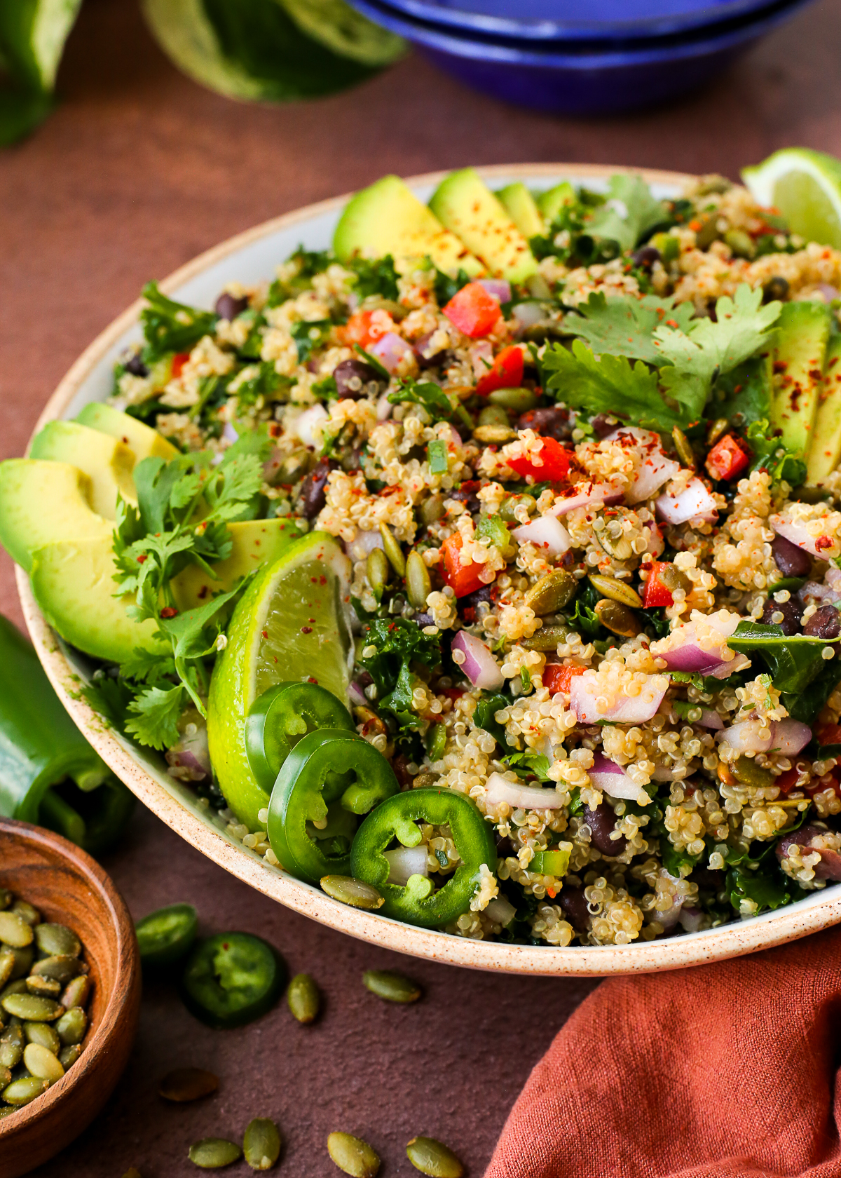 A colorful quinoa salad, garnished with sliced avocados, fresh cilantro, and lime wedges, displayed on a kitchen countertop.
