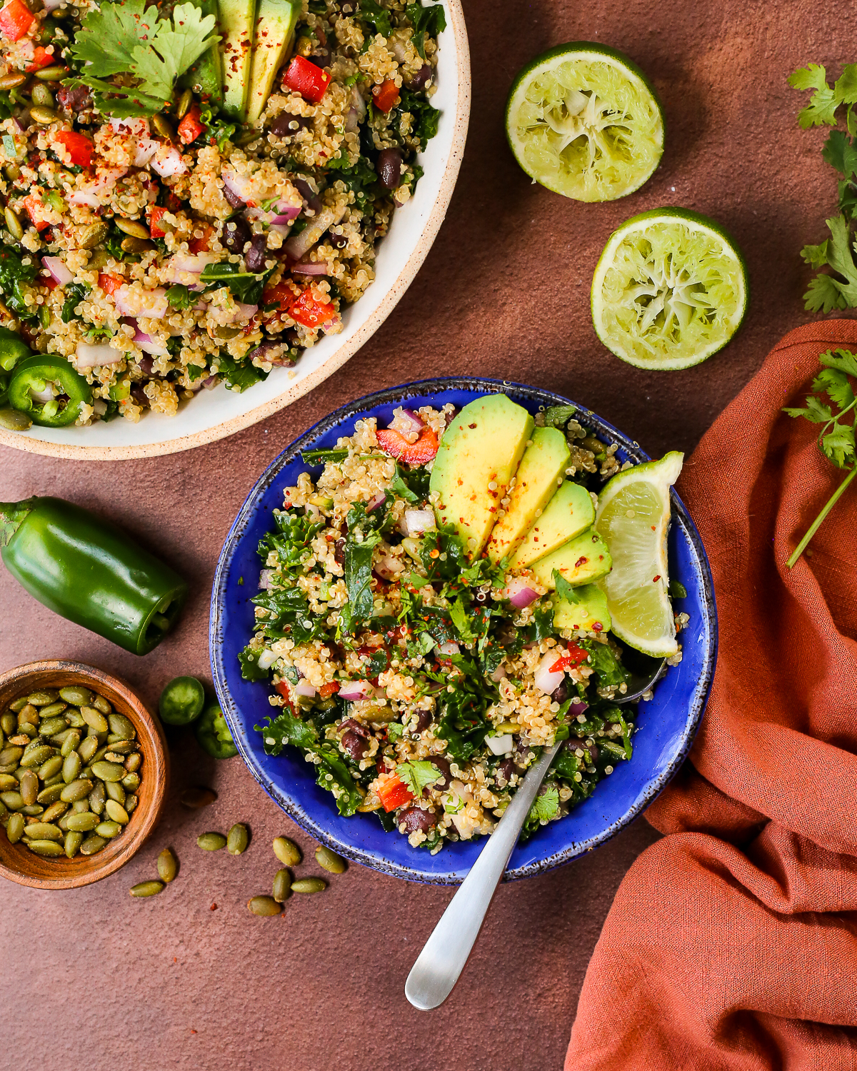 A bright blue ceramic bowl filled with a colorful quinoa salad recipe, garnished with sliced avocado and a lime wedge.