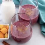 Two fruit smoothies made with mango, berries, and milk in glasses on a kitchen countertop