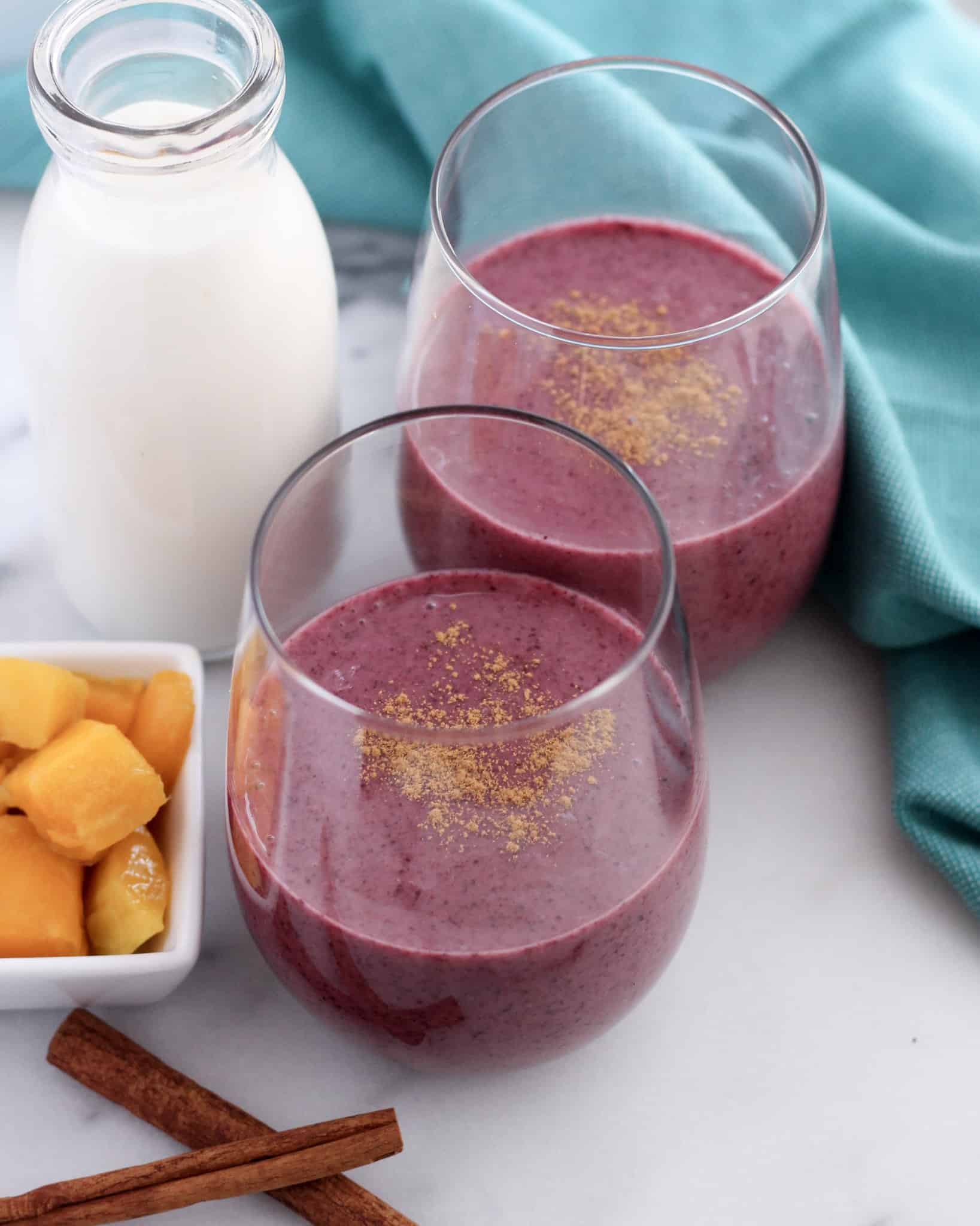 Two fruit smoothies made with mango, berries, and milk in glasses on a kitchen countertop