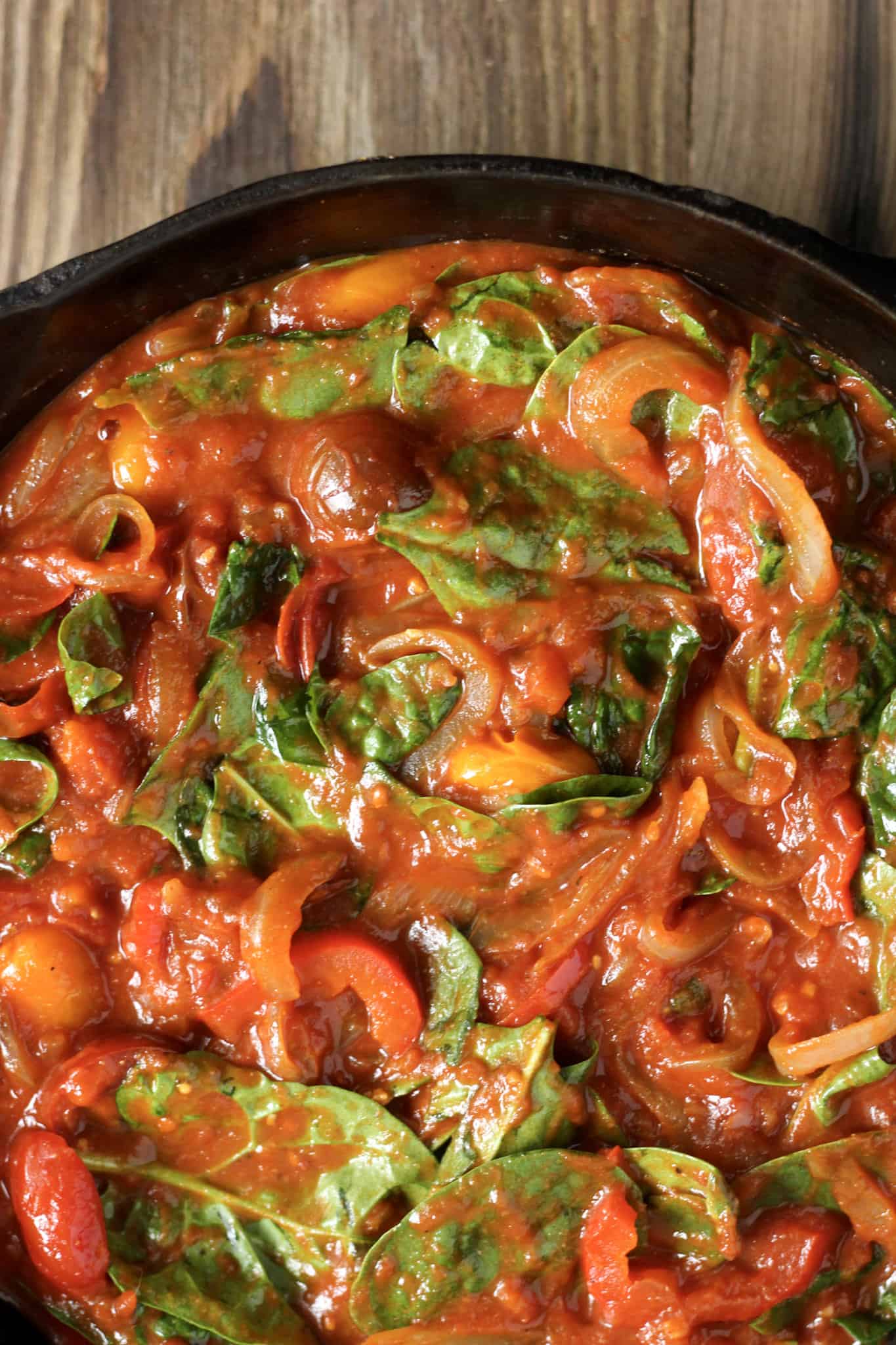 Overhead view of a cast iron skillet with marinara sauce, cooked peppers, onions, and spinach