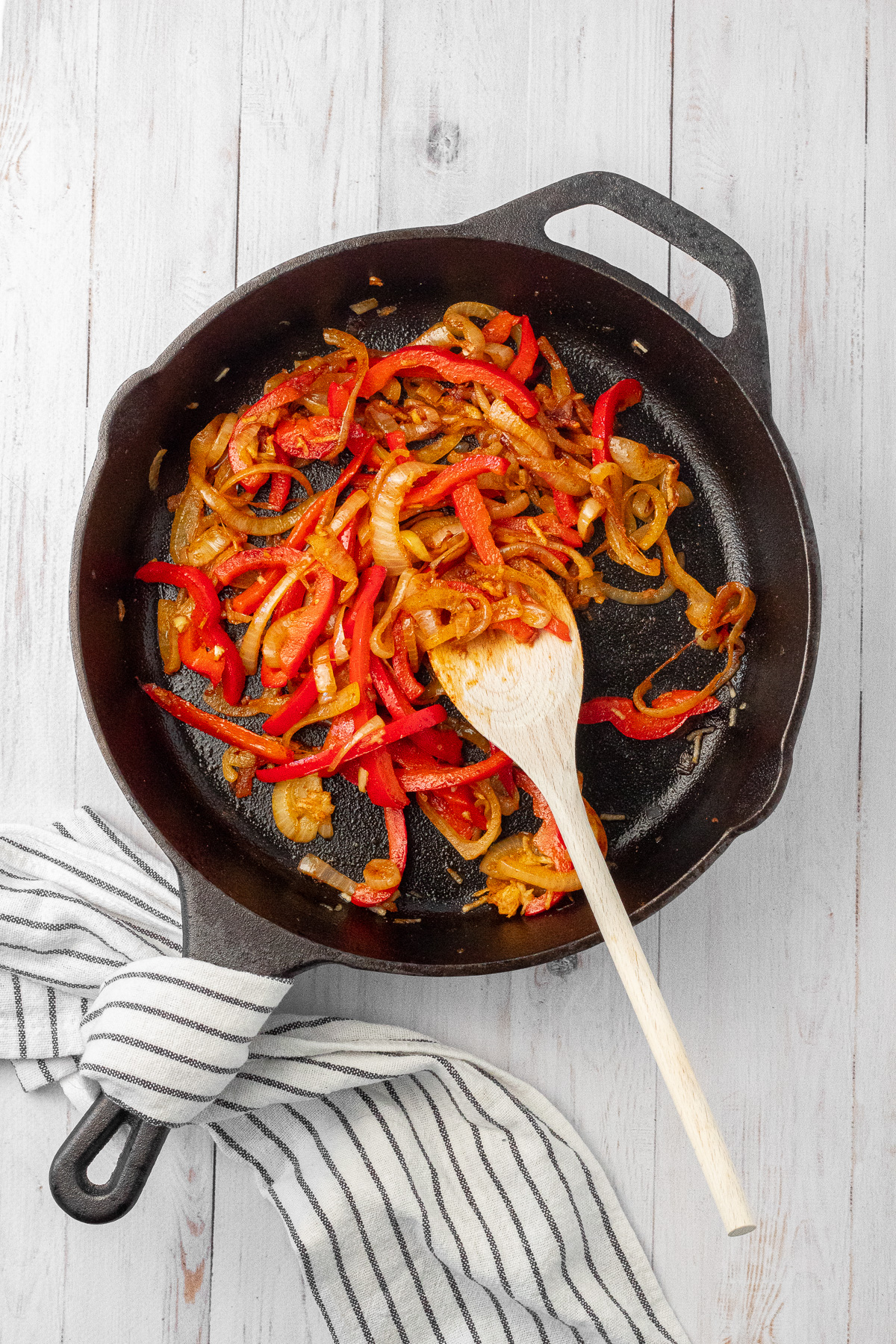 Sliced onions and red bell pepper cooking in a cast iron skillet. 