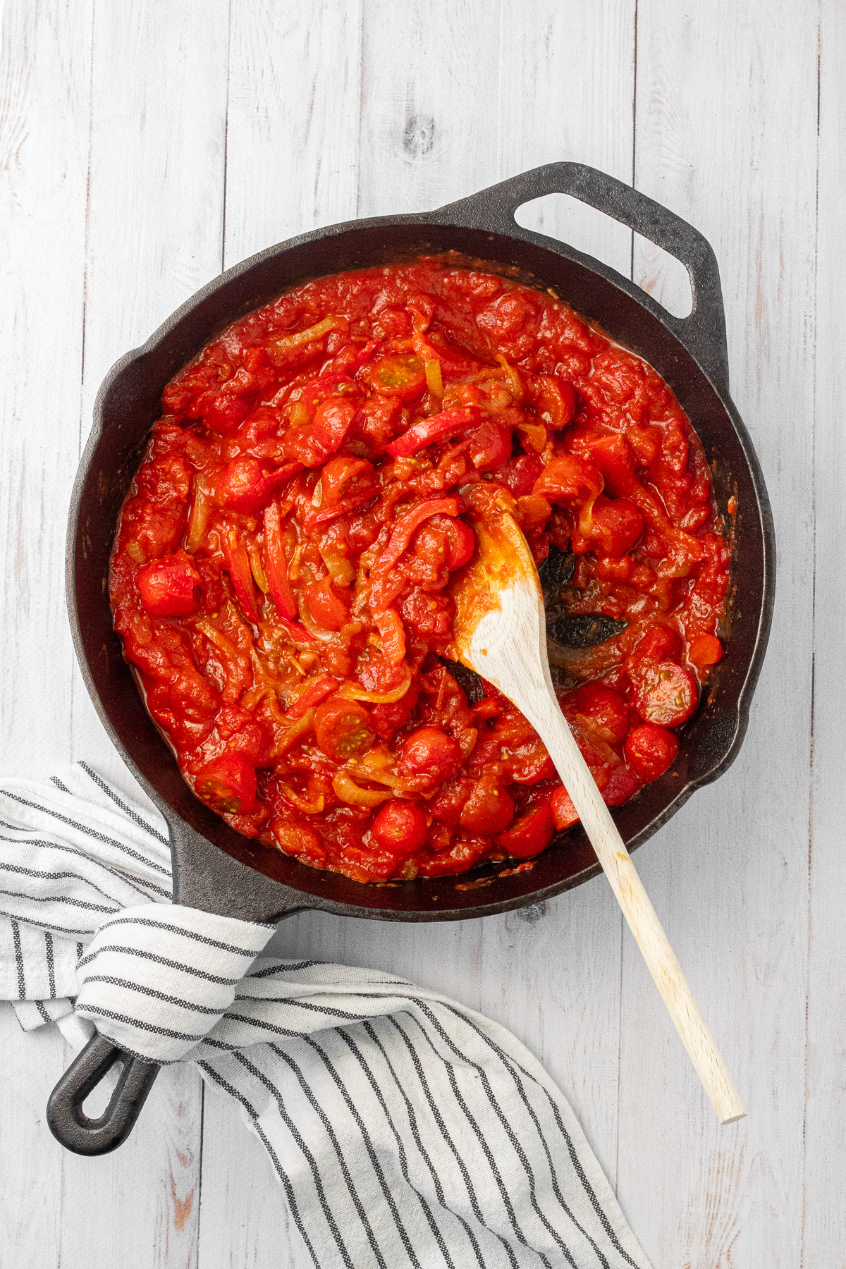 A mixture of cooked onions, red bell pepper, cherry tomatoes, and marinara sauce in a cast iron skillet. 