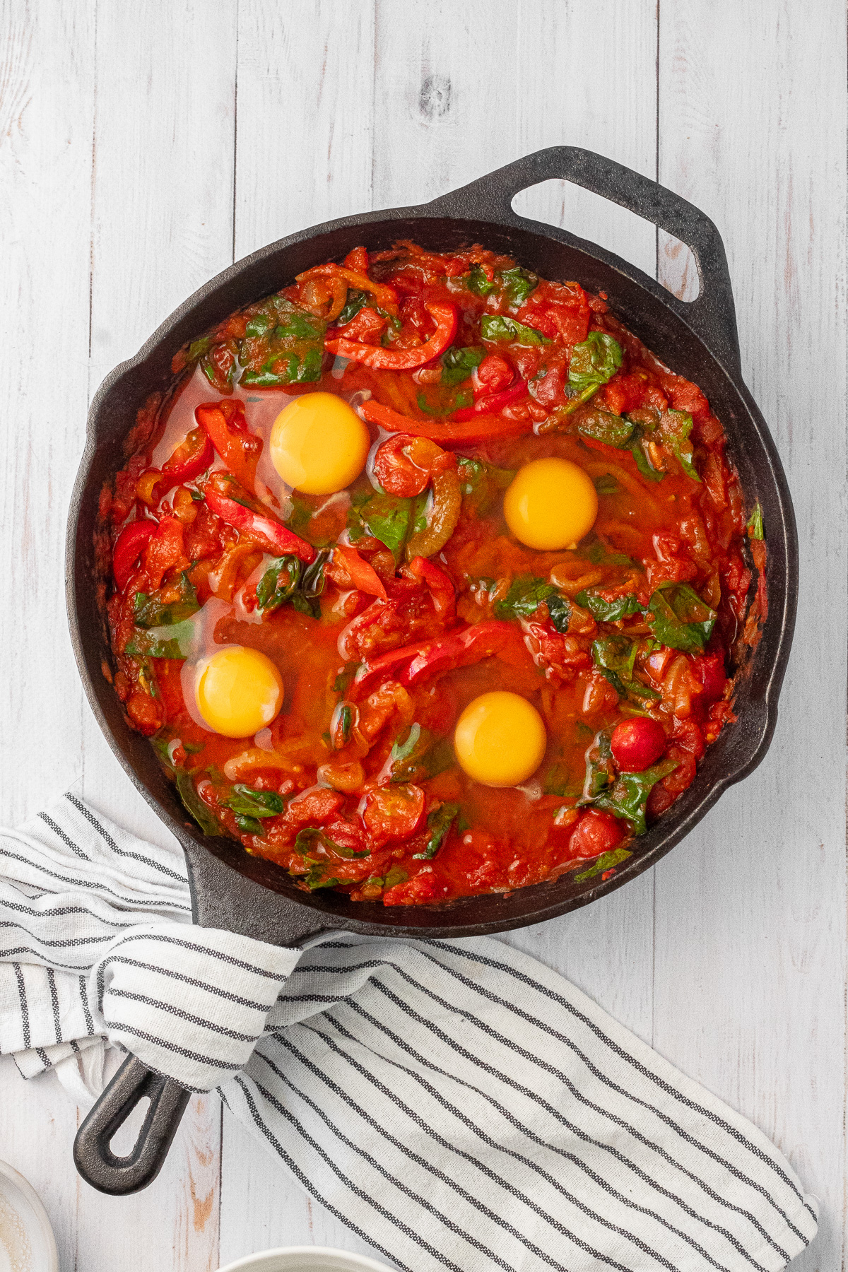 A shakshuka mixture in a cast iron skillet, with eggs carefully dropped on top as it's prepared to bake in the oven. 