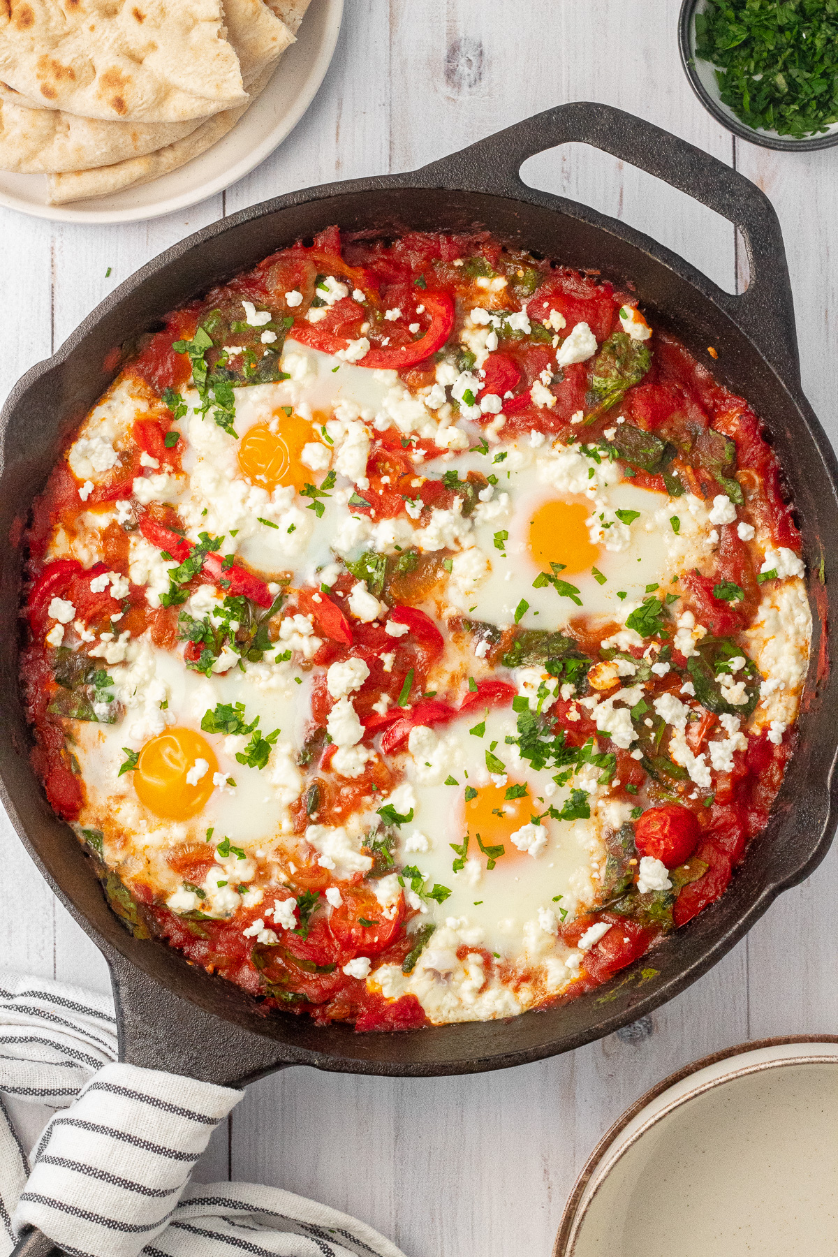 A cast iron skillet filled with a shakshuka recipe, topped with crumbled feta cheese and chopped parsley.
