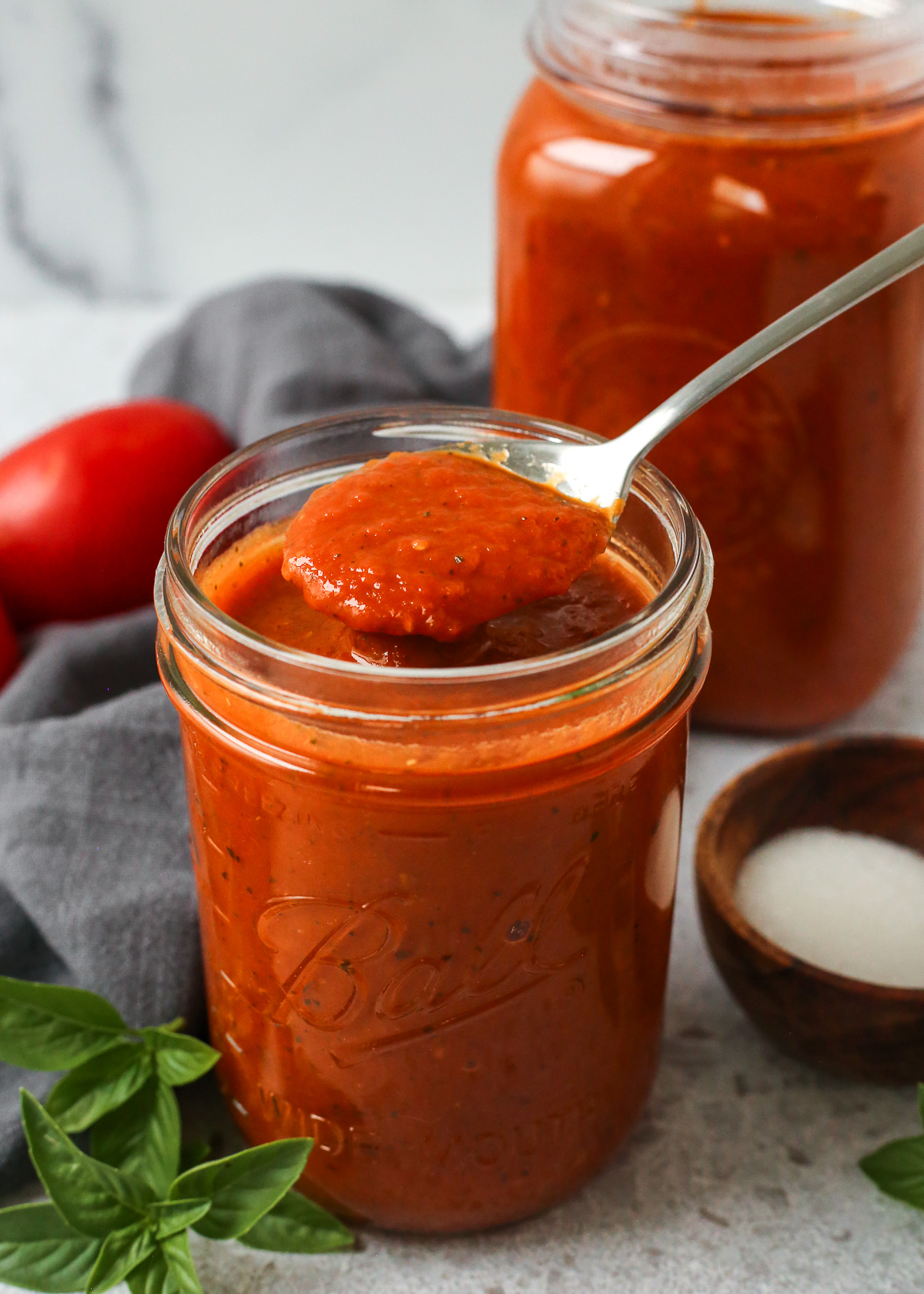 A silver spoon lifts a big scoop of homemade marinara sauce from a glass mason jar to show the thick texture and rich, red color.