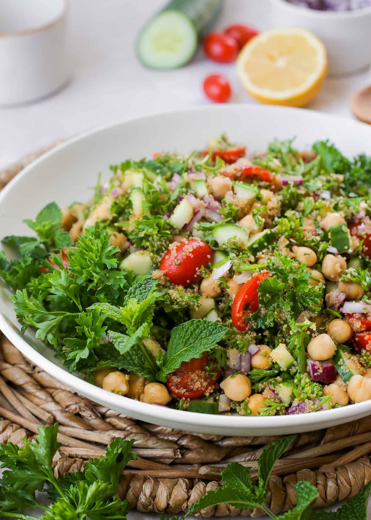 A large serving bowl filled with amaranth tabbouleh, served on a kitchen countertop with extra lemons and vegetables in the background.