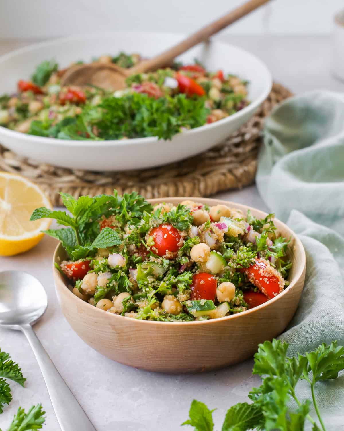 A wooden bowl filled with amaranth tabbouleh, topped with fresh parsley with a serving bowl in the background.