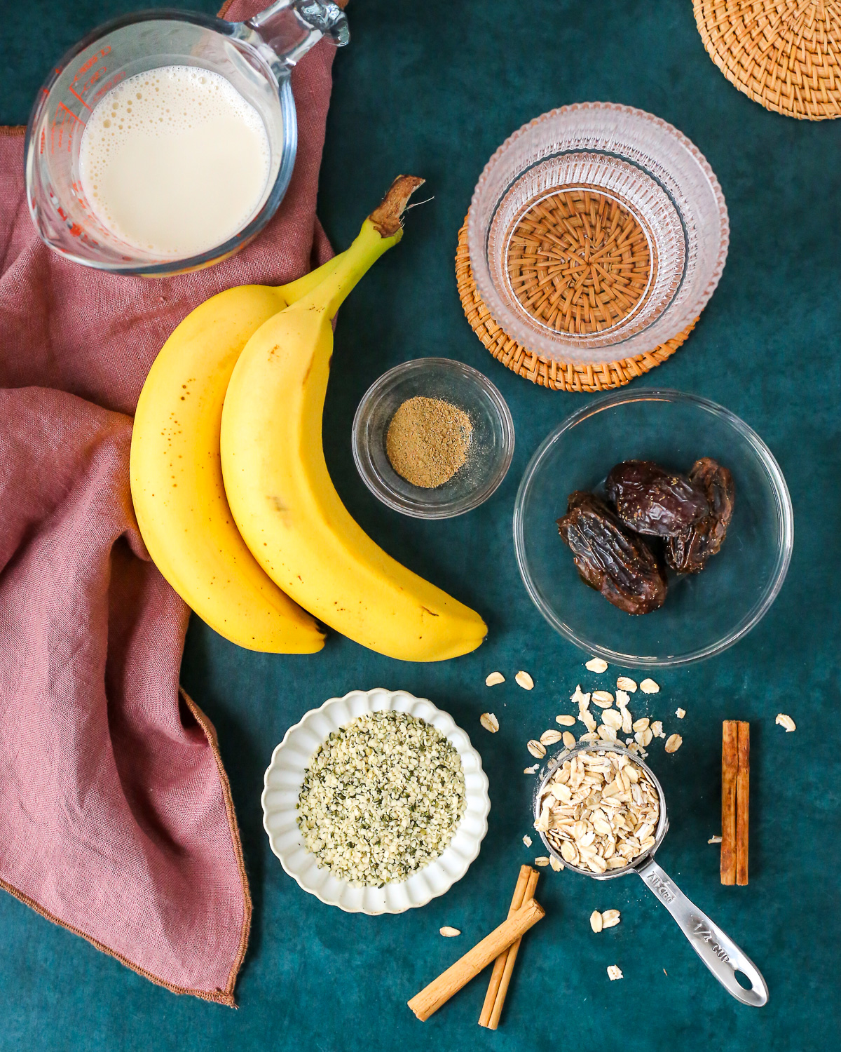 An assortment of ingredients to make a high fiber banana chai smoothie, including bananas, oats, hemp hearts, oat milk, dates, and chai spice blend. 