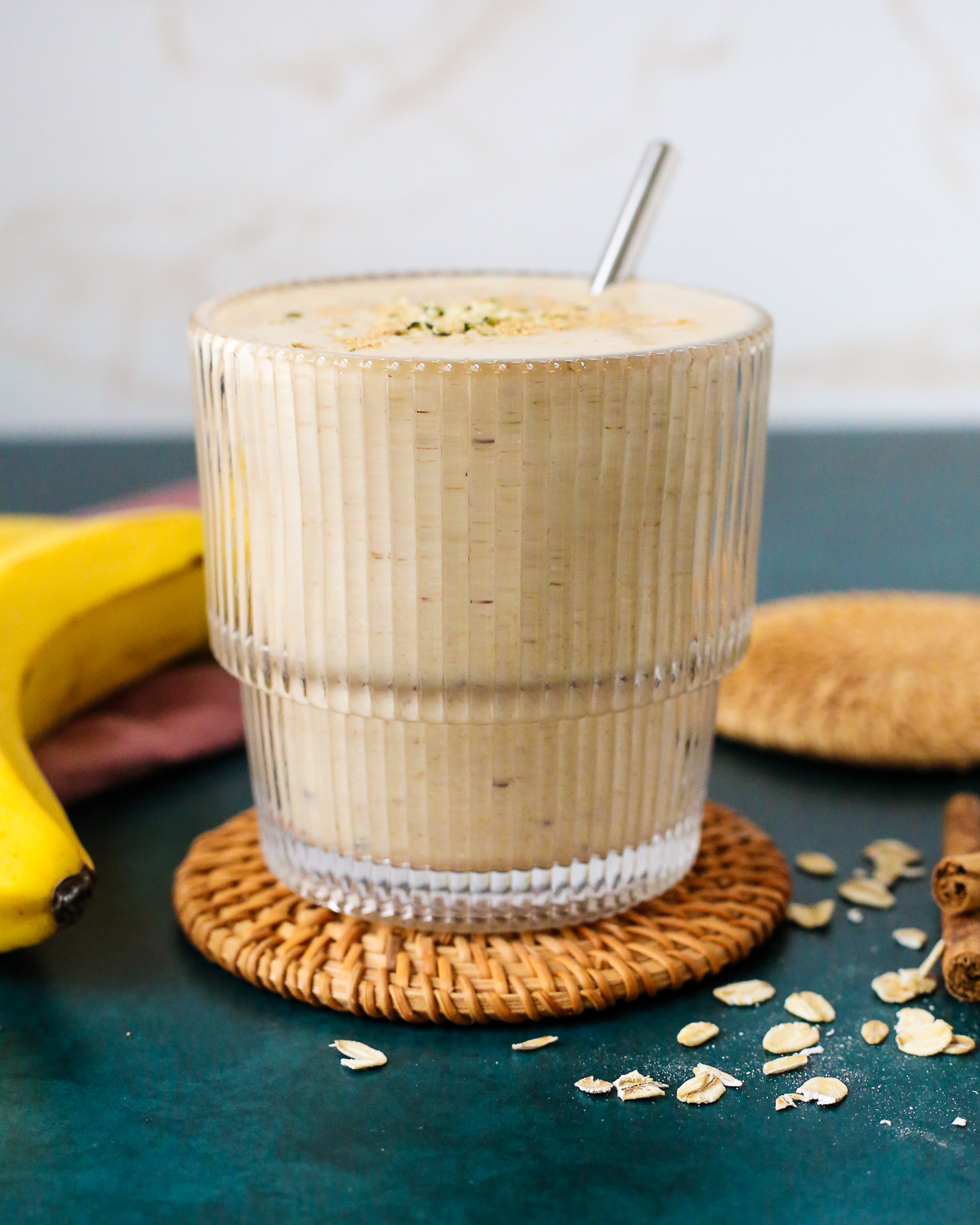 A banana chai smoothie served in a clear glass with a short metal straw. 