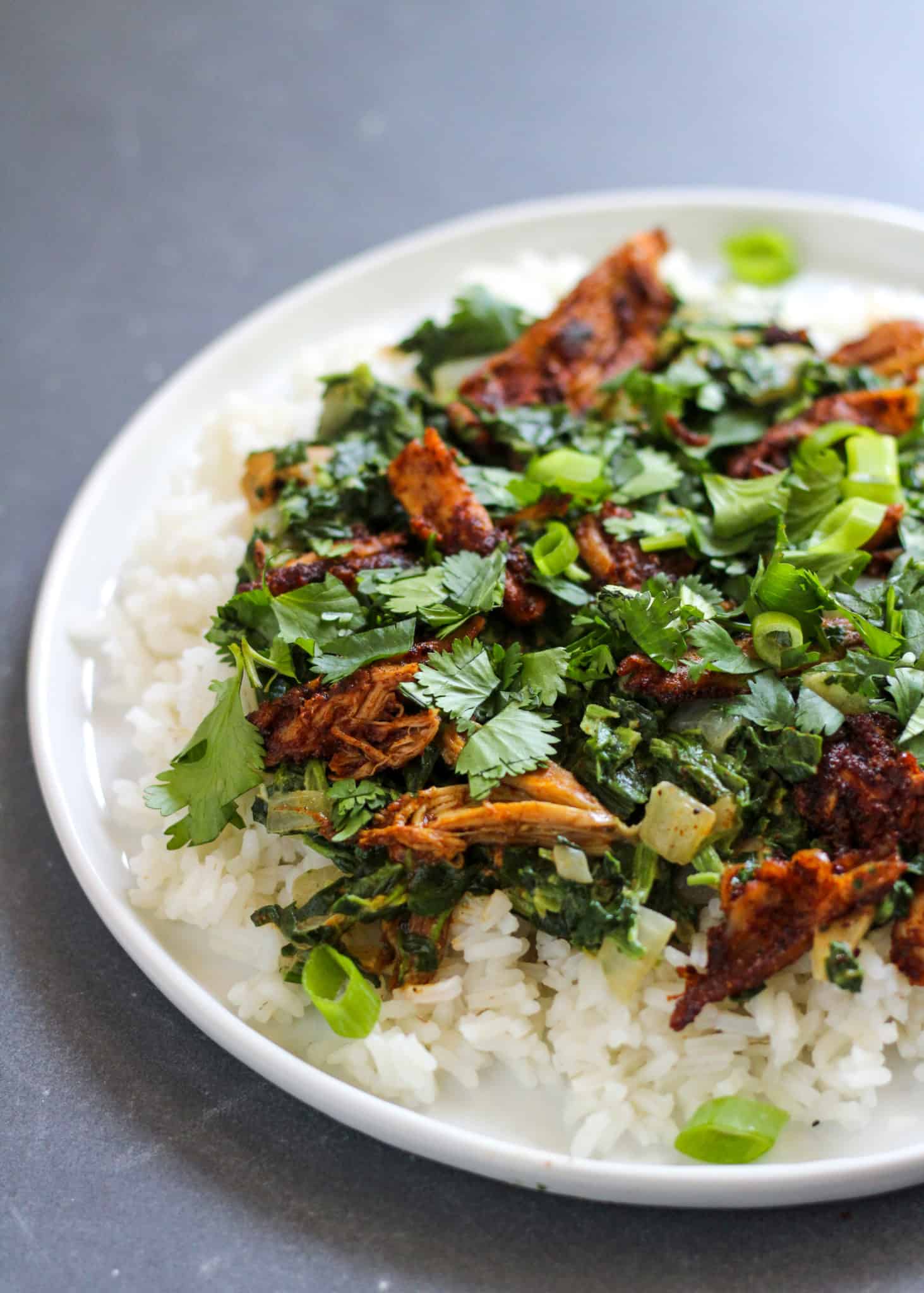 A white plate filled with rice topped with cooked rotisserie-style chicken, spinach, and cilantro