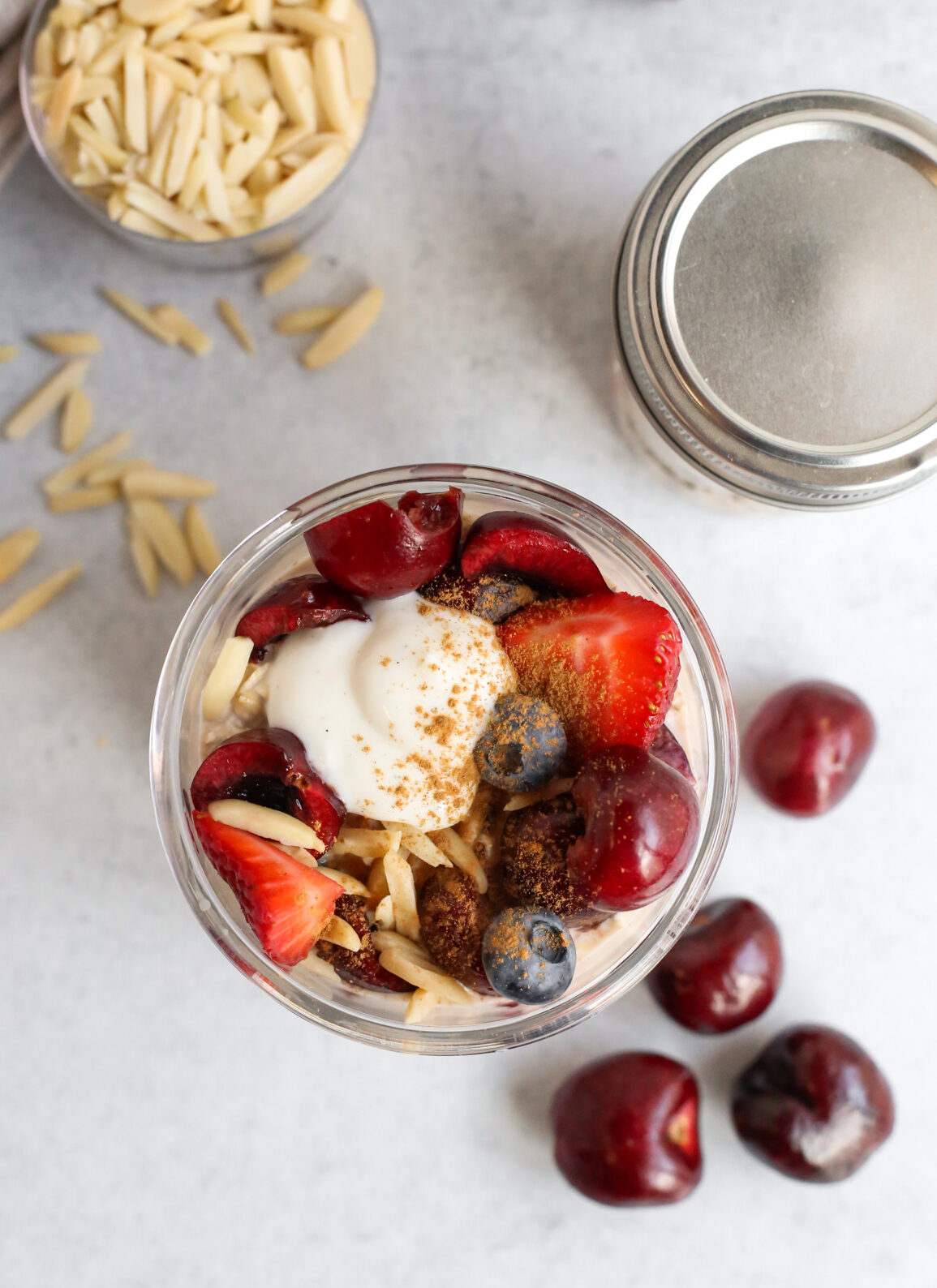 Overhead view of a container of Berry Cherry Almond Overnight Oats, served in a small glass jar on a stone kitchen countertop