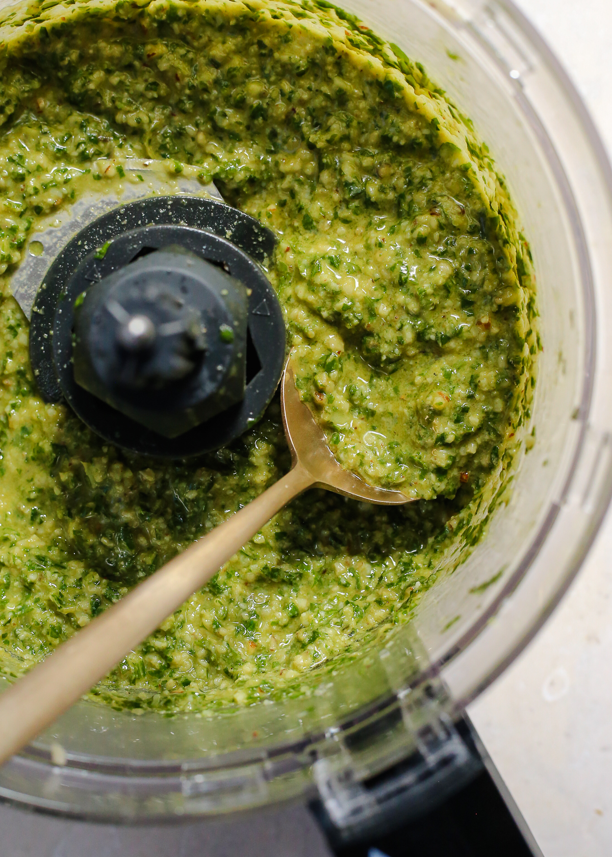 A view into the bowl of a food processor containing freshly made homemade pesto, with a thick texture and vibrant green color. 
