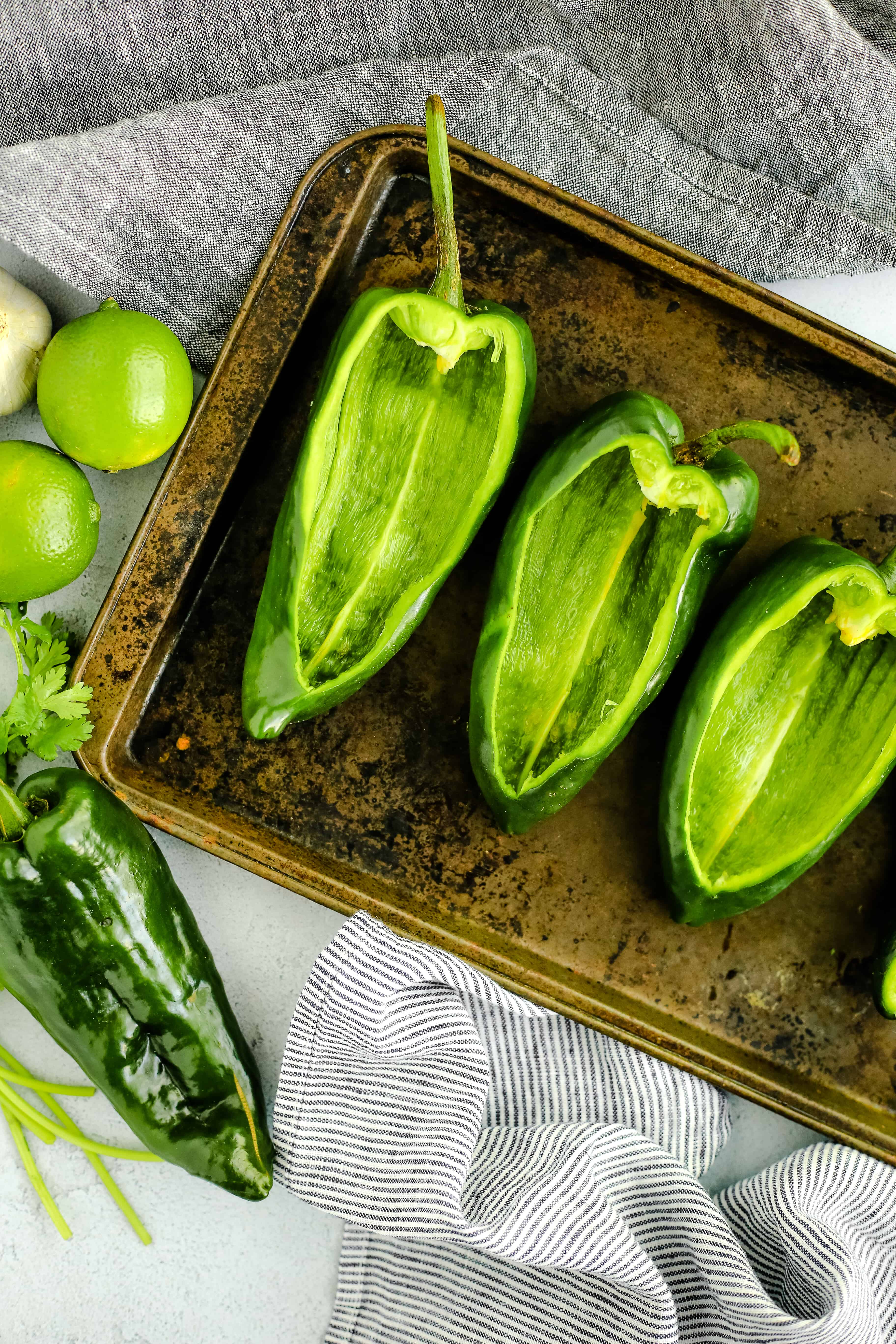 Sliced and de-seeded green poblano peppers arranged on a rustic metal sheet pan in prepared to make stuffed peppers