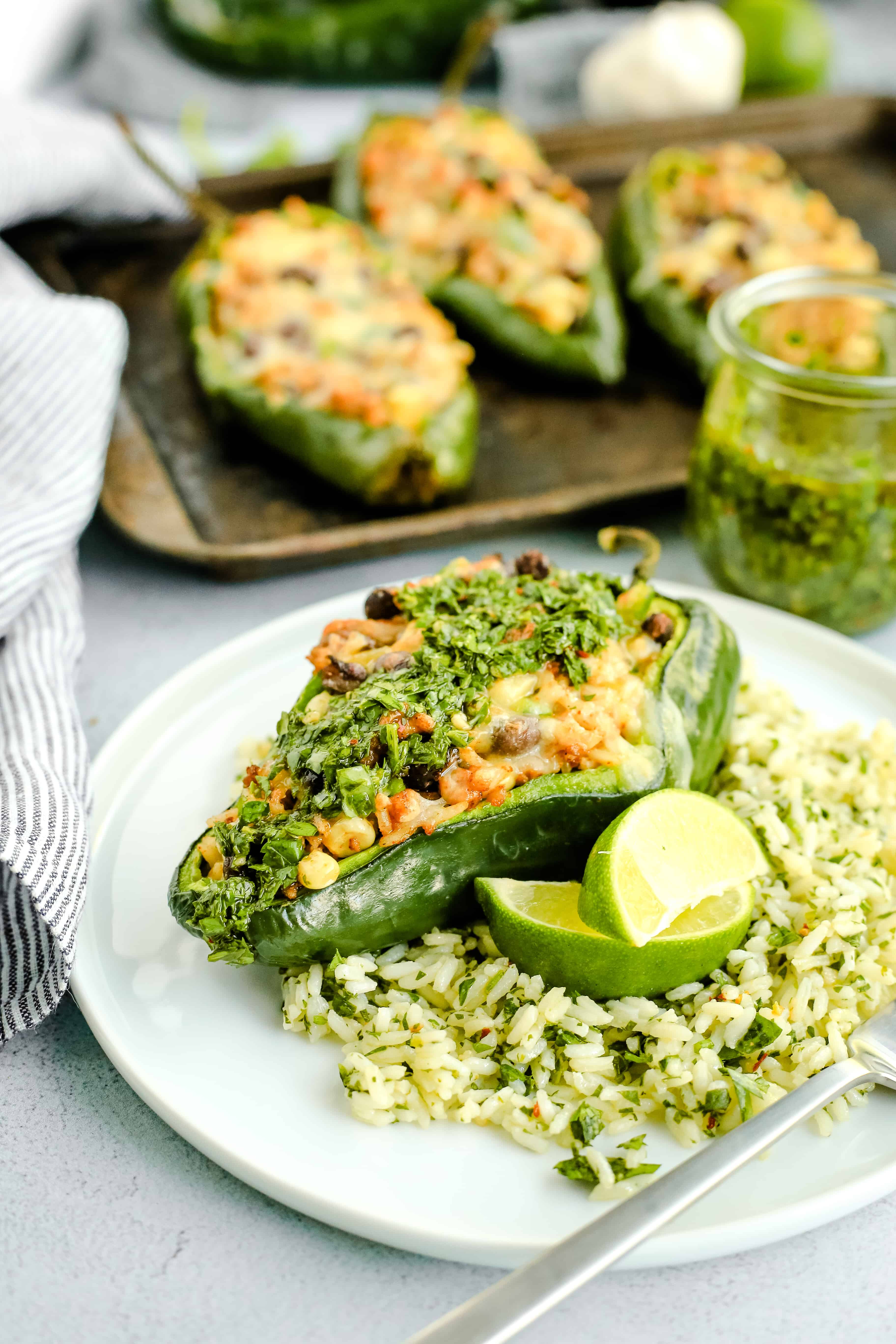 Image of Stuffed Poblano Peppers with Chimichurri Rice and Chorizo, with extra herbs and lime wedges for garnish, served on a white ceramic plate on a kitchen countertop