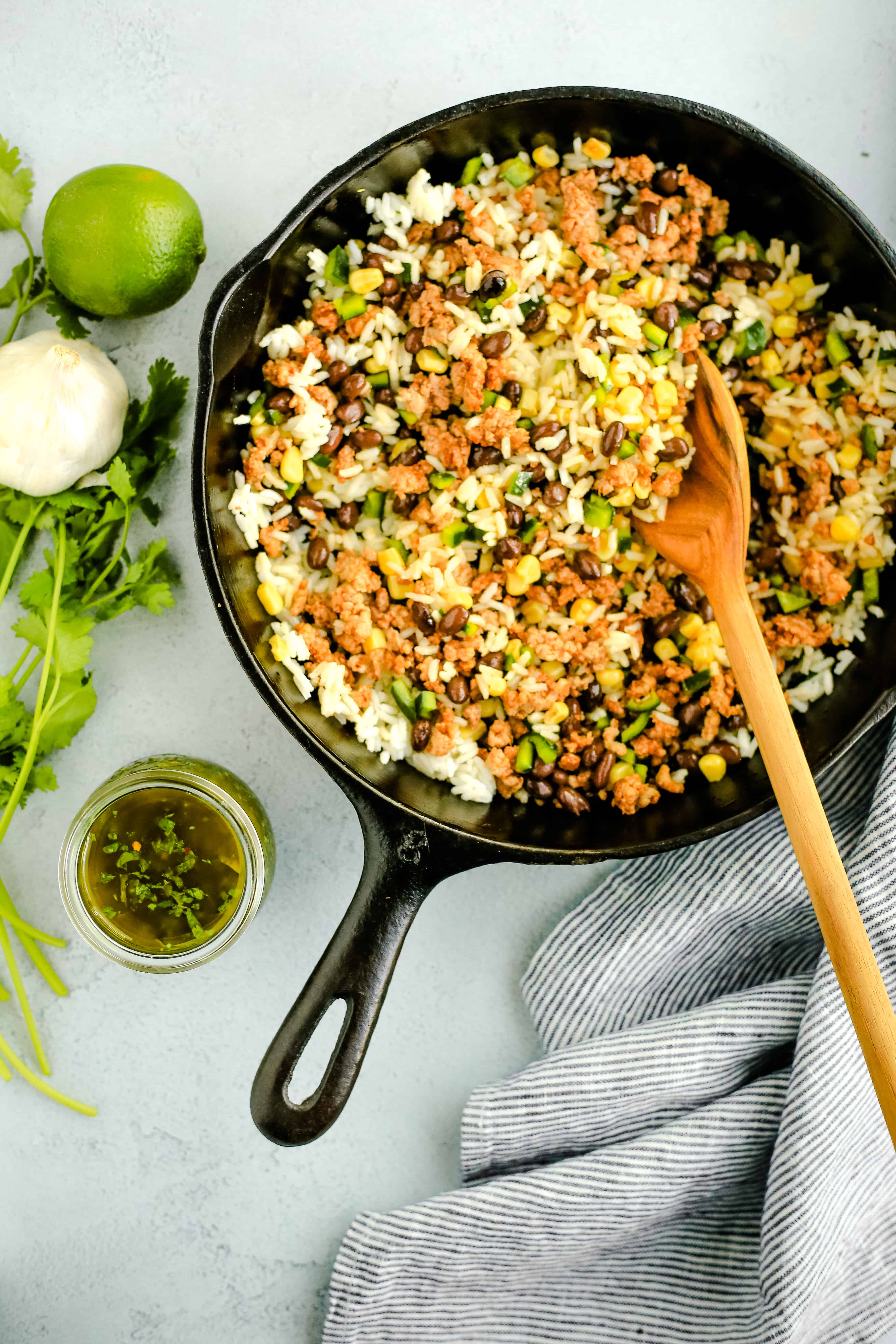 Overhead view of a black cast iron skillet filled with cooked rice, ground chorizo, black beans, corn, and diced peppers, with a wooden serving spoon to stuff the mixture into poblano peppers