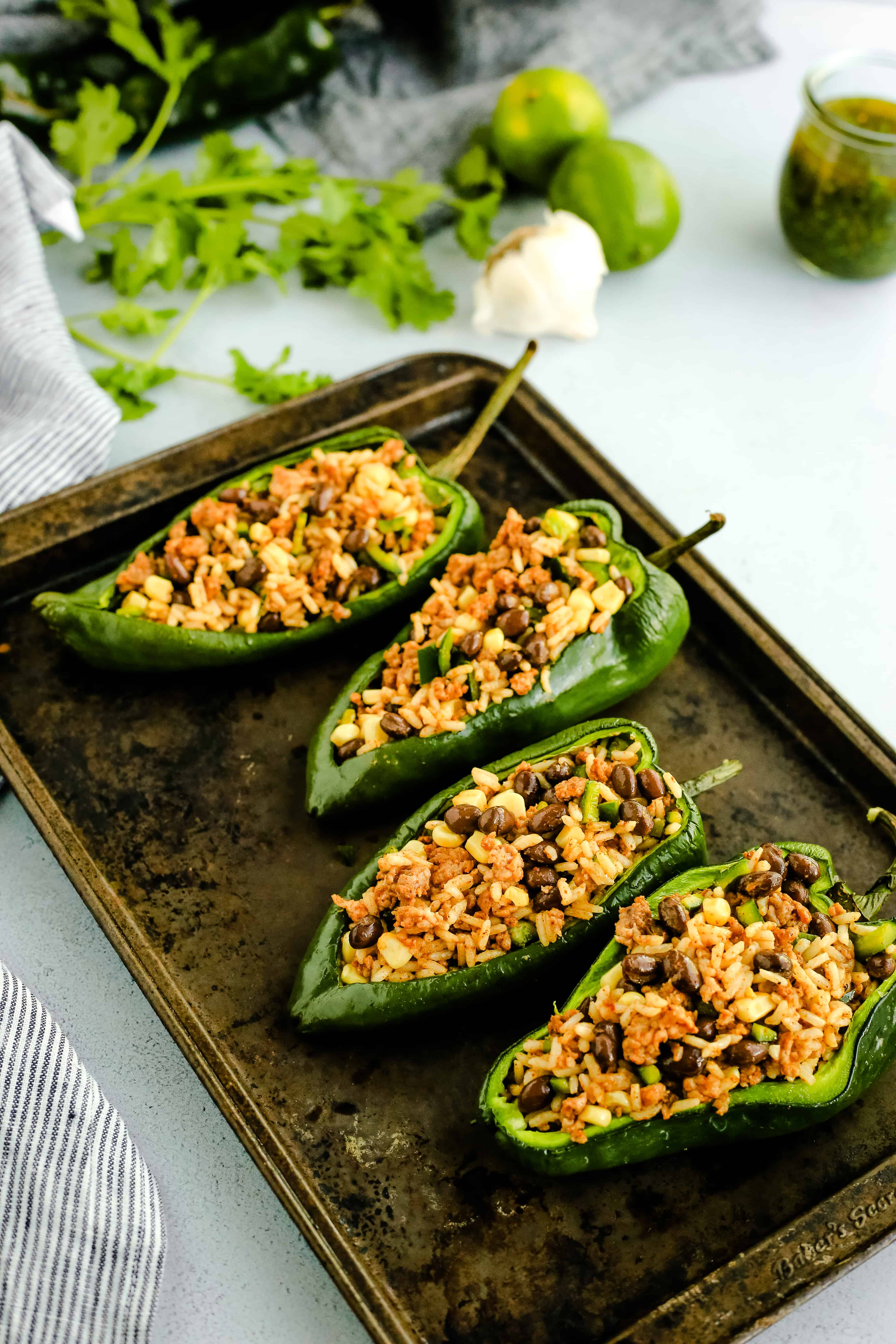 Angled view of stuffed poblano peppers filled with the mixture of cooked white rice, chorizo, black beans, corn, and vegetables, prior to being baked in the oven