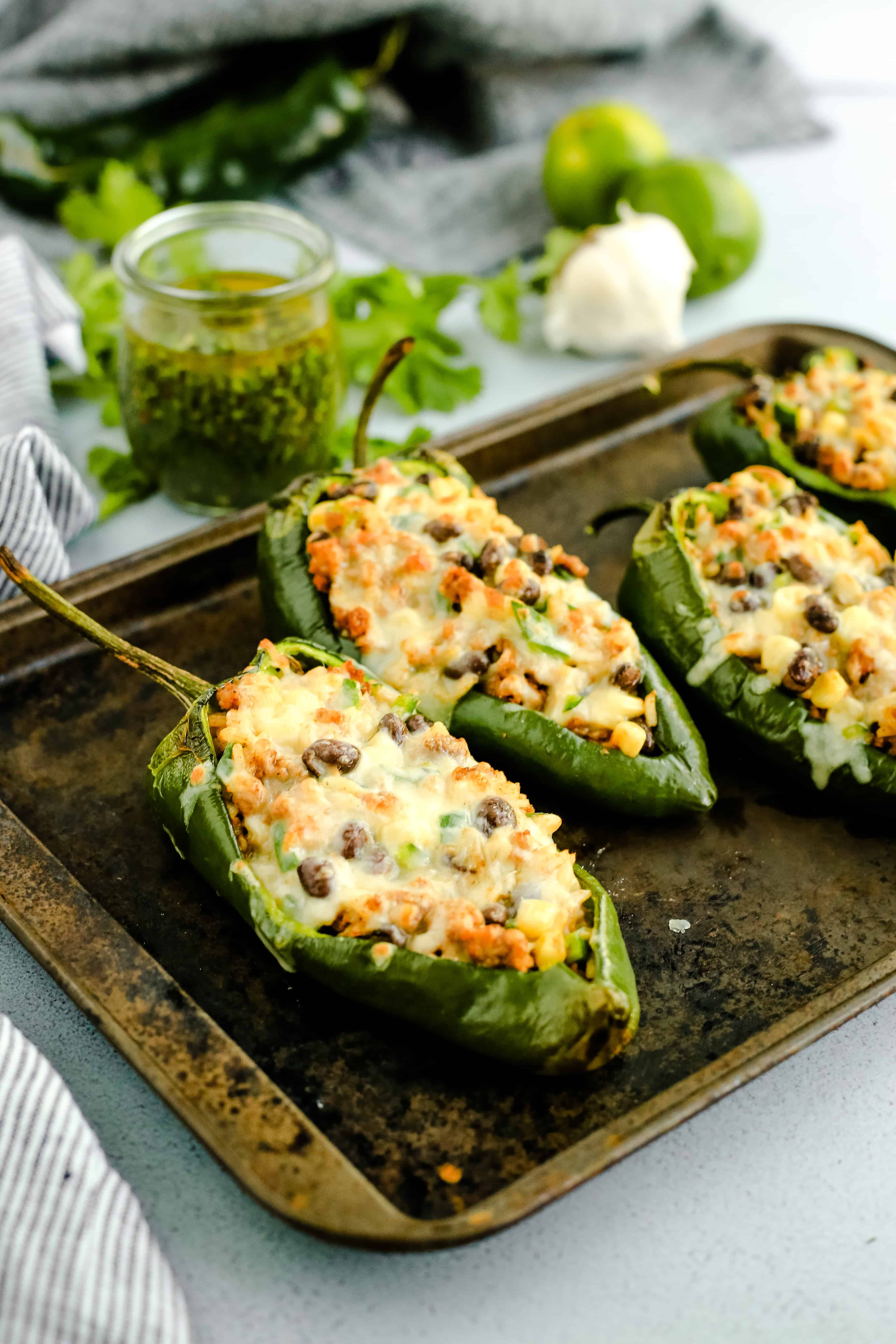 Angled view of stuffed poblano peppers covered with melted cheese, arranged on a metal sheet pan after cooking so the cheese is melted and slightly browned on top