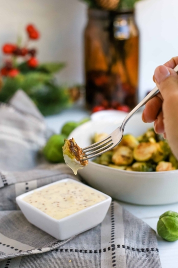 A woman's hand holds a fork and dips a roasted Brussels sprout into a creamy dipping sauce