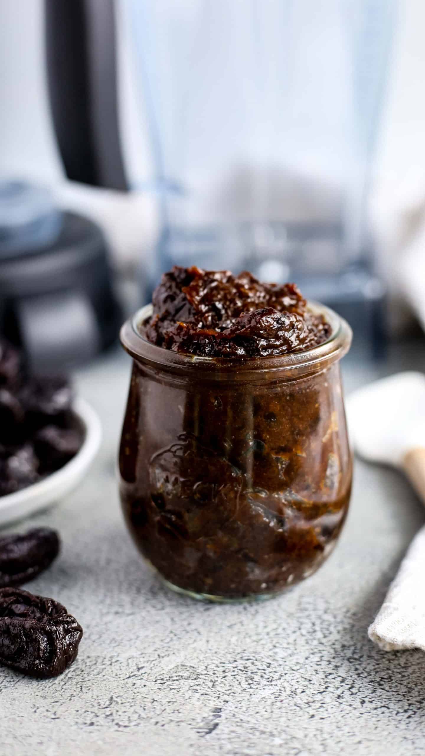 Small glass jar of a  Prune Puree Recipe with blender in the background