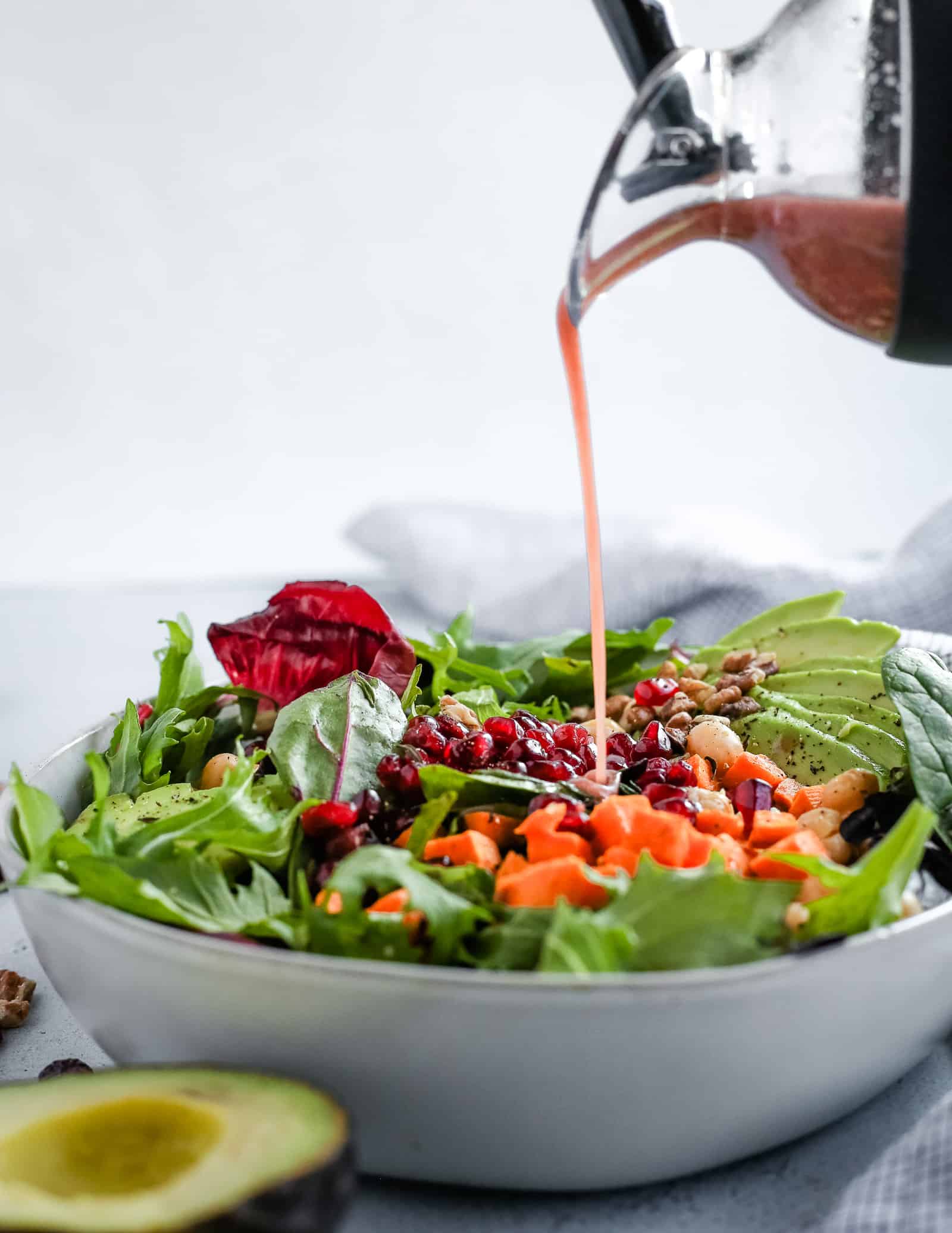 Colorful salad with a salad dressing shaker pouring a creamy pomegranate dressing on top