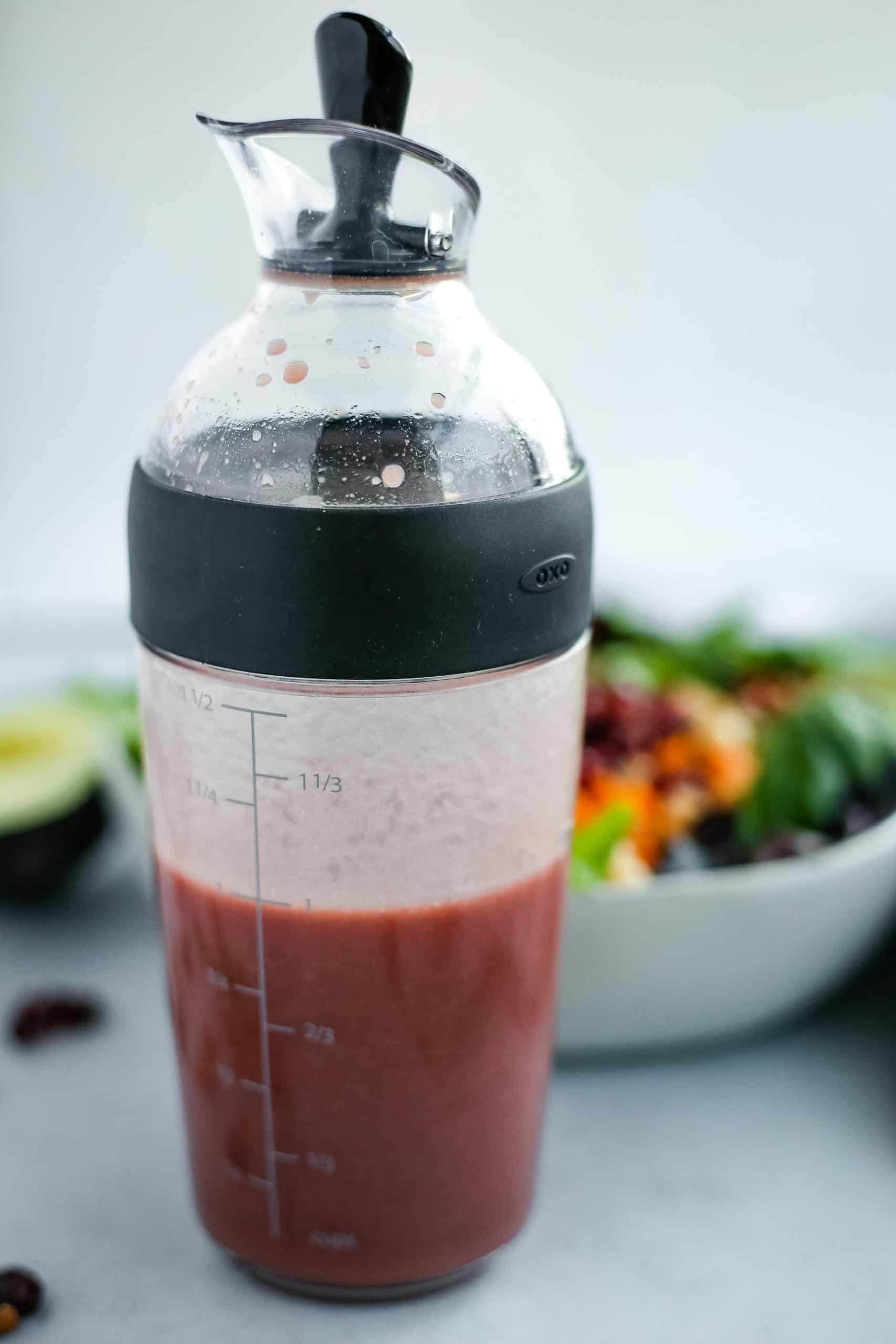 Salad shaker with DIY creamy pomegranate dressing with colorful salad in the background