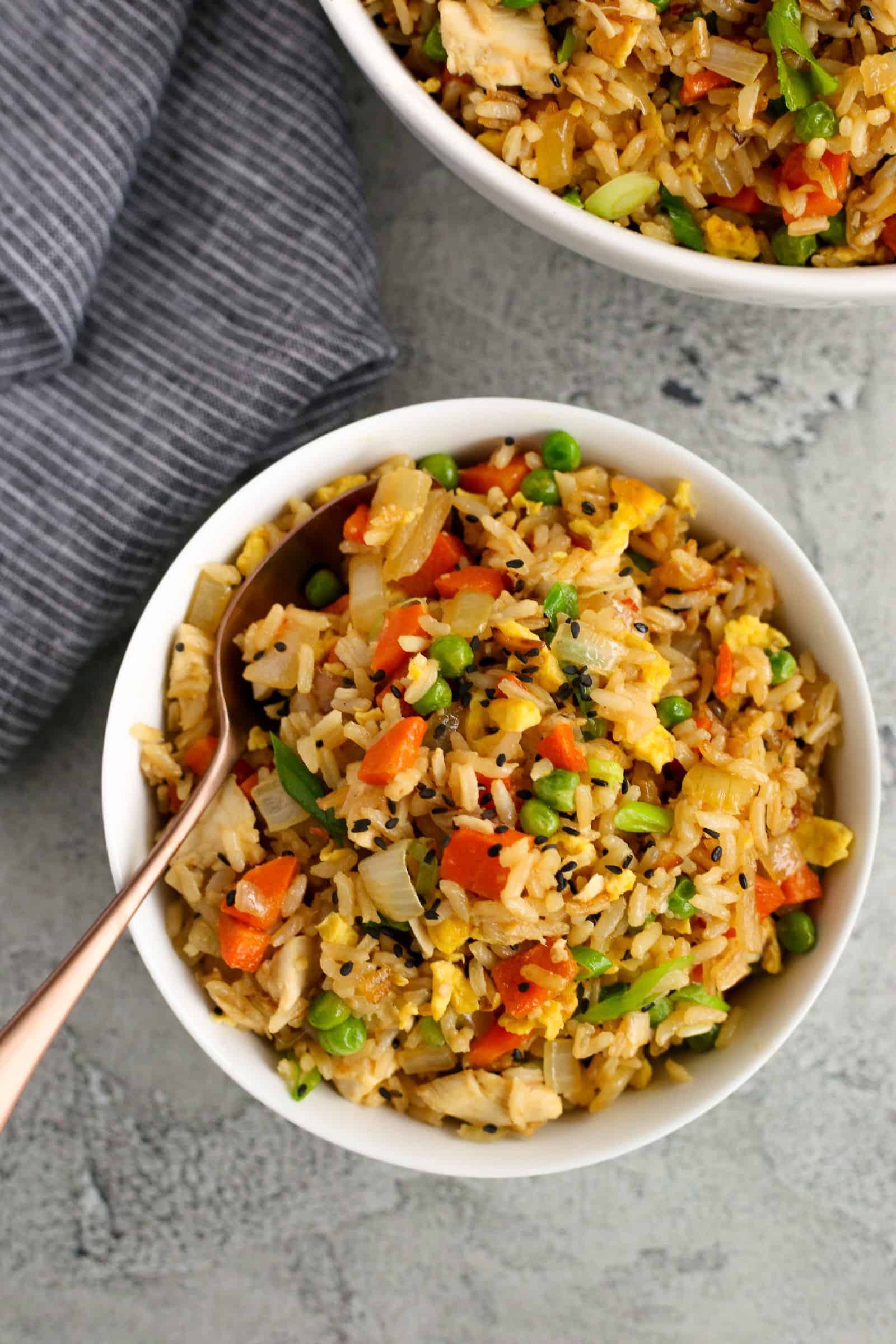 Overhead view of a bowl filled with rotisserie chicken fried rice, with onions, carrots, peas, and eggs mixed throughout