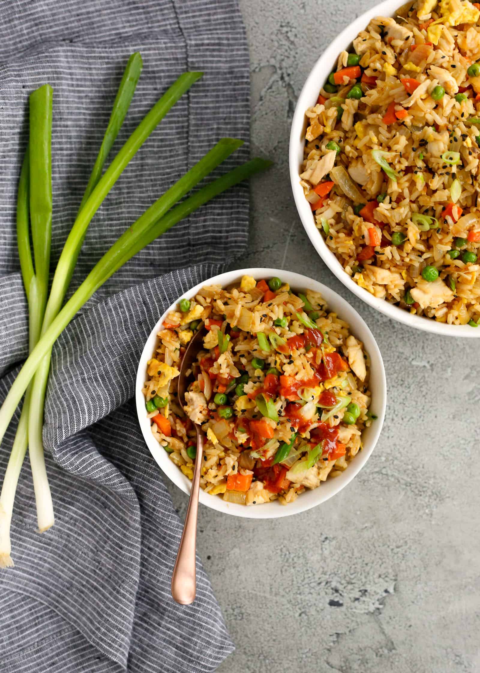 Two bowls of fried rice with leftover rotisserie chicken, veggies, sriracha, and green onions