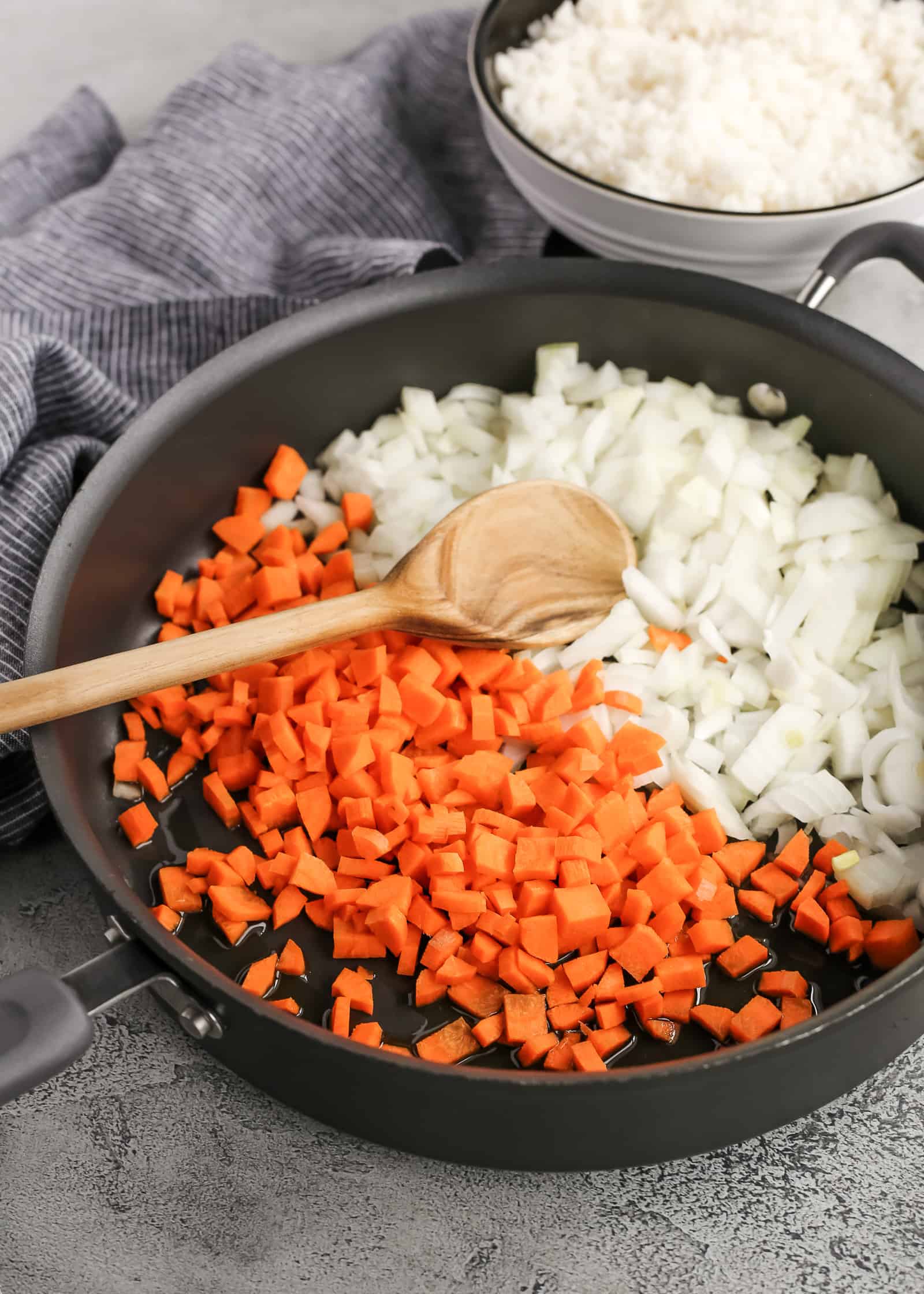 Large skillet with chopped carrots and diced onions, appearing ready to be cooked on a stovetop with a small amount of oil added to the pan