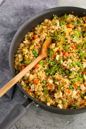 Large frying pan of weeknight fried rice with wooden spoon and blue linen