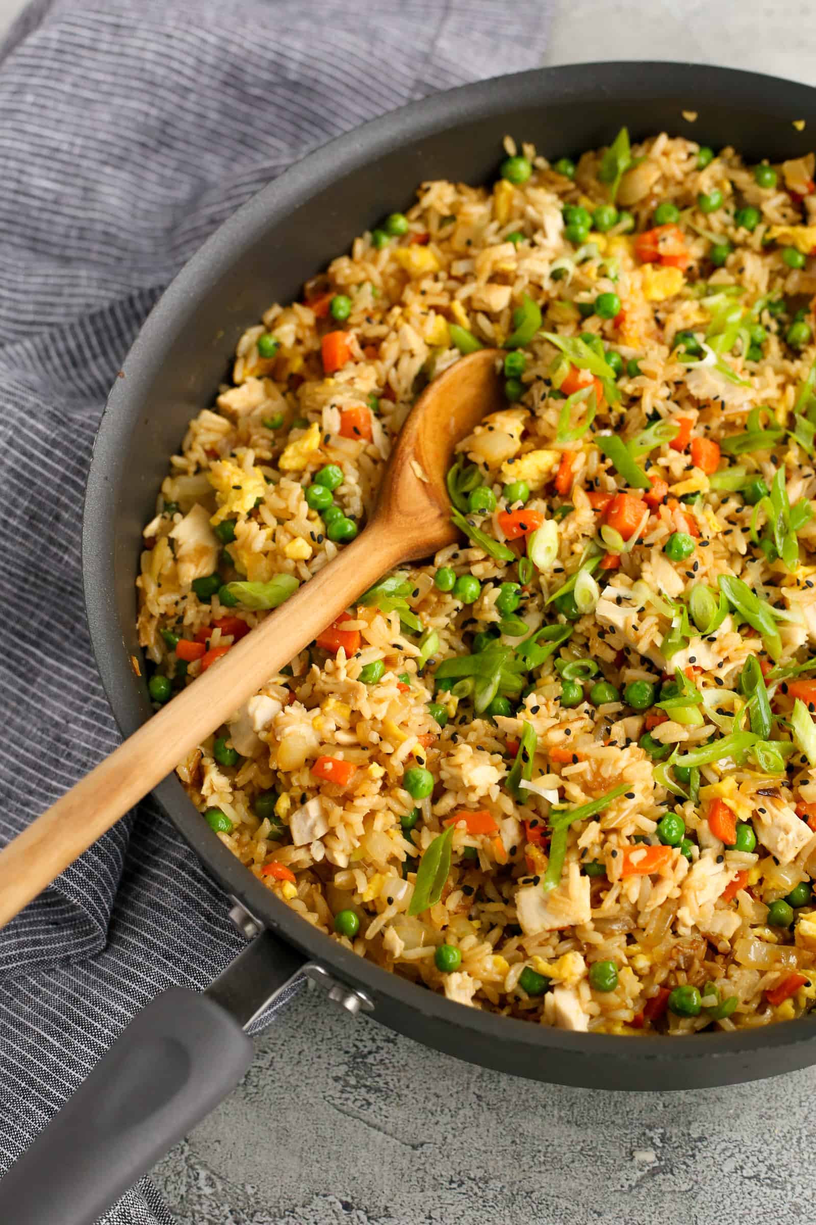 Large frying pan of rotisserie chicken fried rice with a wooden serving spoon resting on the side