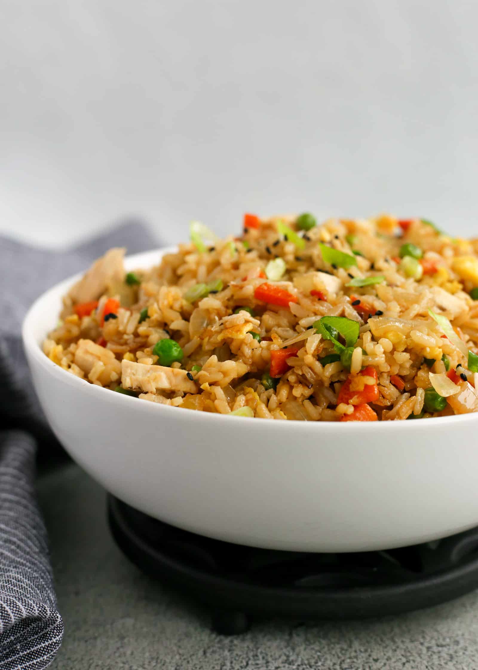 White serving bowl on a trivet, filled high with an easy fried rice recipe with leftover rotisserie chicken, carrots, and green peas