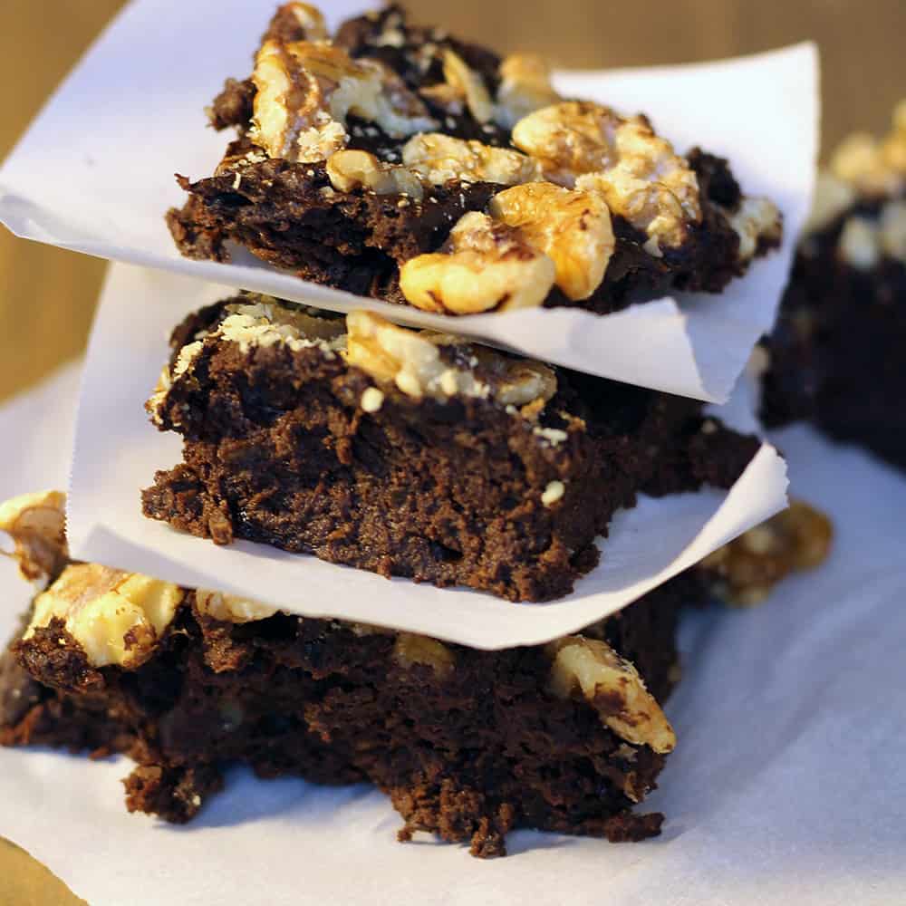 A stack of three chocolate brownies with walnuts separated with parchment paper