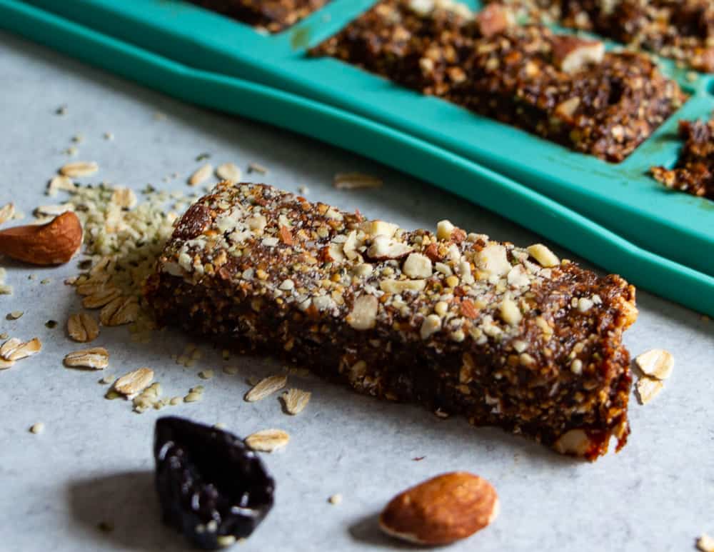 A prune bar with the no-bake mold in the background and prunes and nuts scattered around it