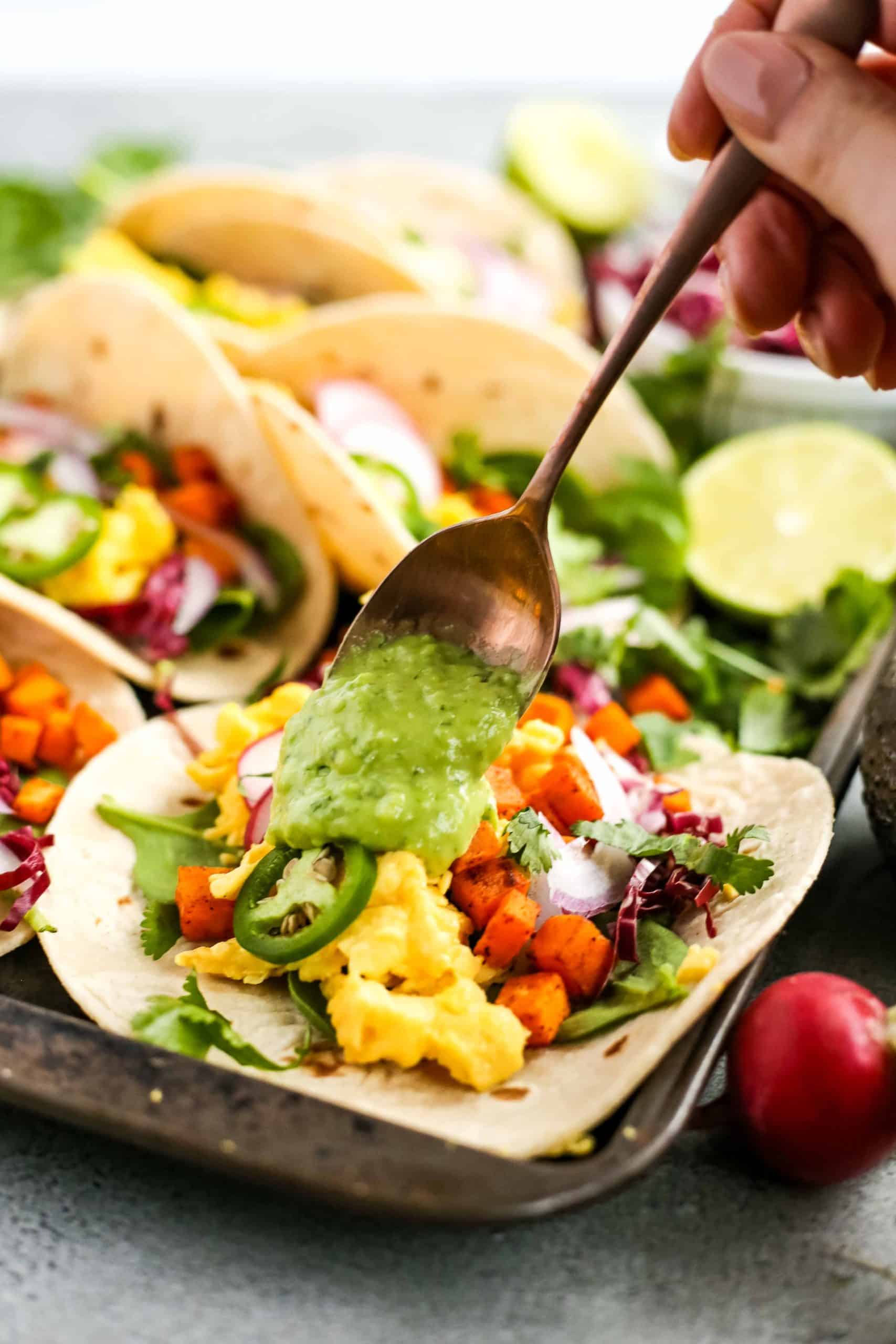 A creamy avocado sauce on top of a colorful scrambled egg taco