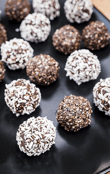 Energy balls on a baking sheet, coated with coconut flakes and chopped nuts