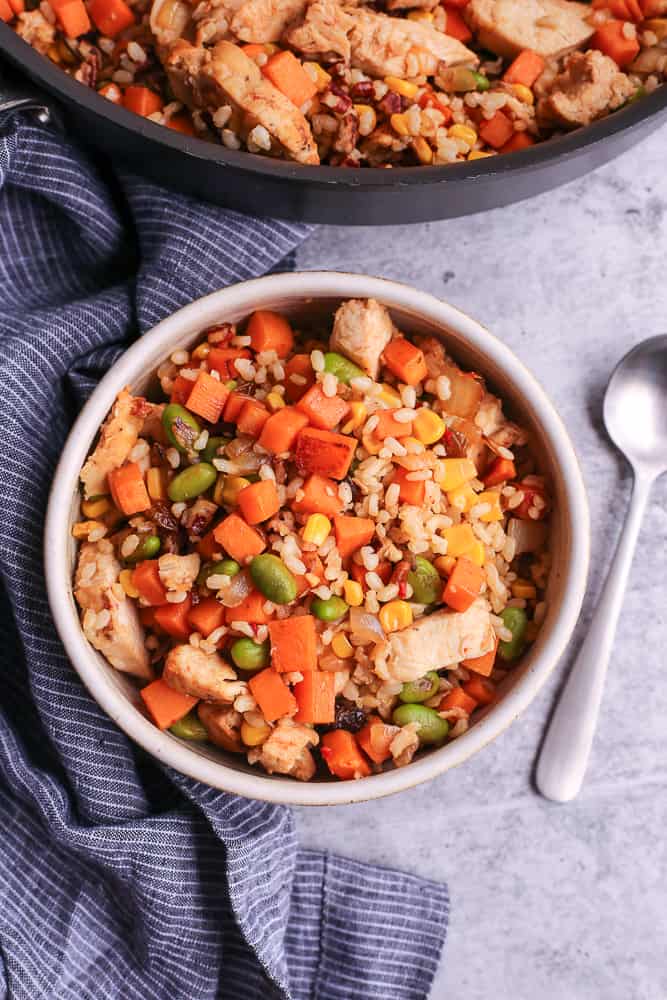 Brown rice and sweet potato hash in a ceramic bowl with silver spoon and skillet