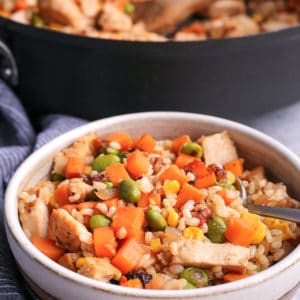 Brown rice and sweet potato hash in a bowl placed in front of a skillet and serving spoon