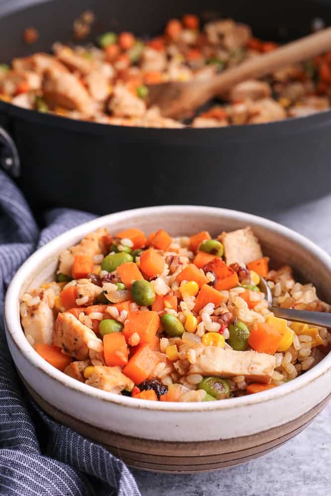 Brown rice and sweet potato hash in a bowl placed in front of a skillet and serving spoon