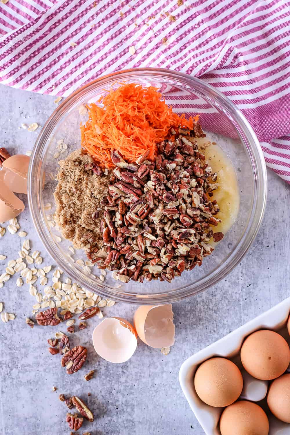 Overhead view of glass mixing bowl with ingredients for spiced carrot cake oat muffins