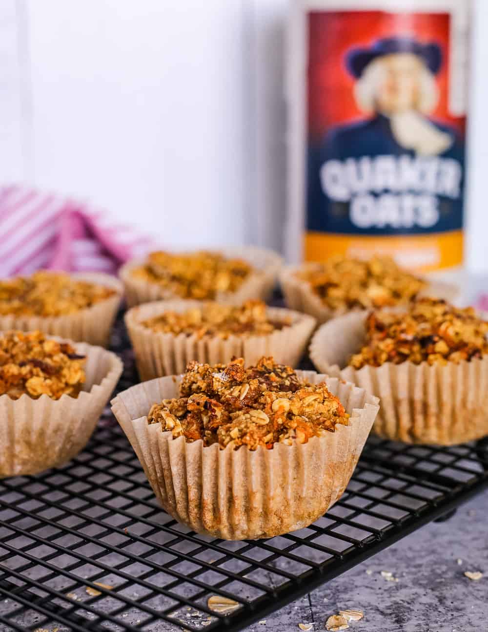 Spiced Carrot Cake Oat Muffins on a cooling rack in front of a canister of Quaker oats