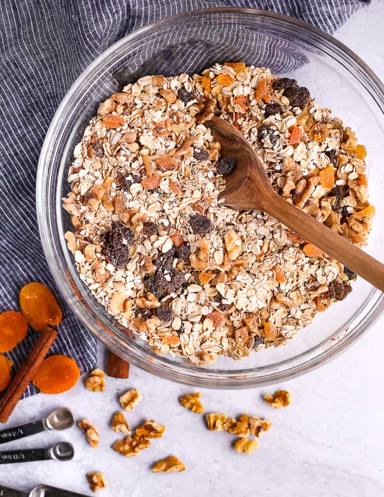 Overhead view of mixed homemade muesli ingredients with measuring spoons on a light grey background