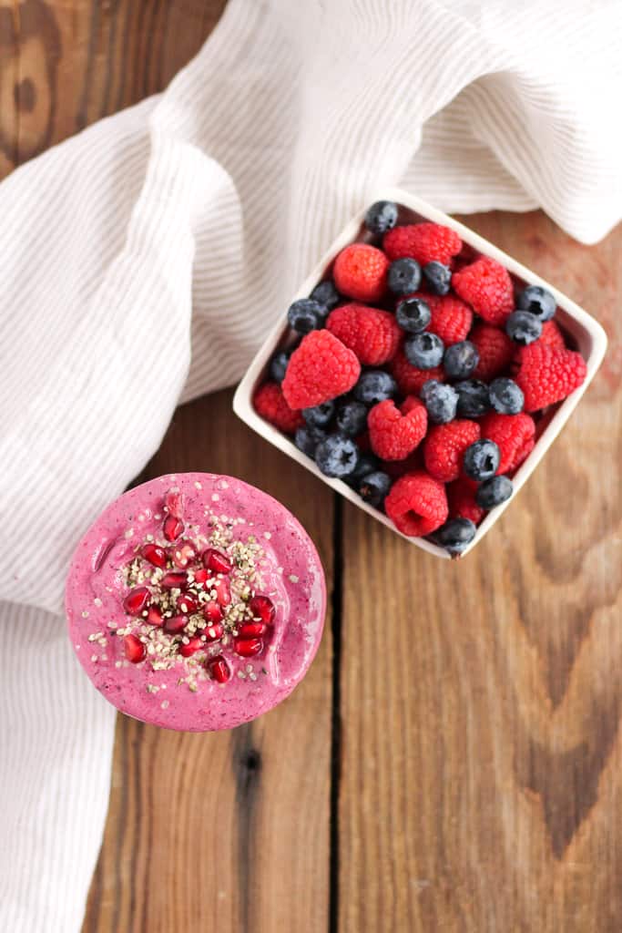 Overhead view of a Pomegranate Berry Smoothie next to fresh raspberries and blueberries