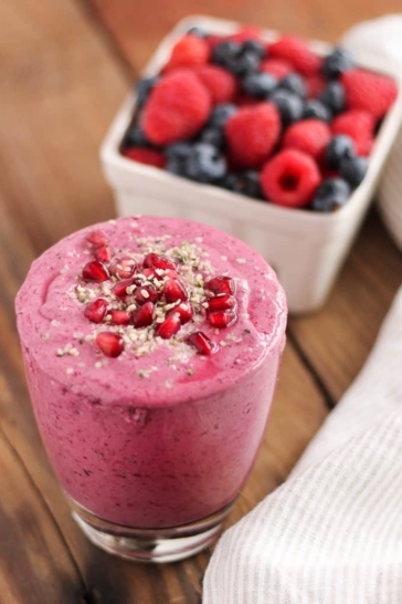 Pomegranate Berry Smoothie in front of a container of fresh raspberries and strawberries