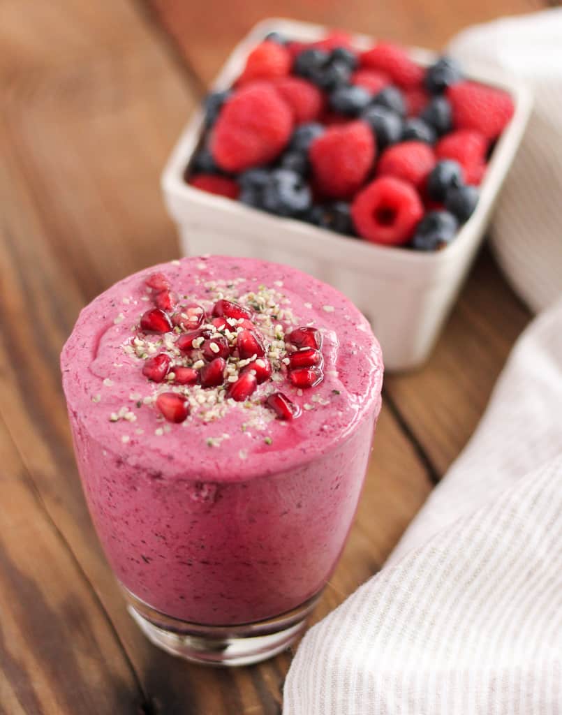 Pomegranate Berry Smoothie in front of a container of fresh raspberries and strawberries